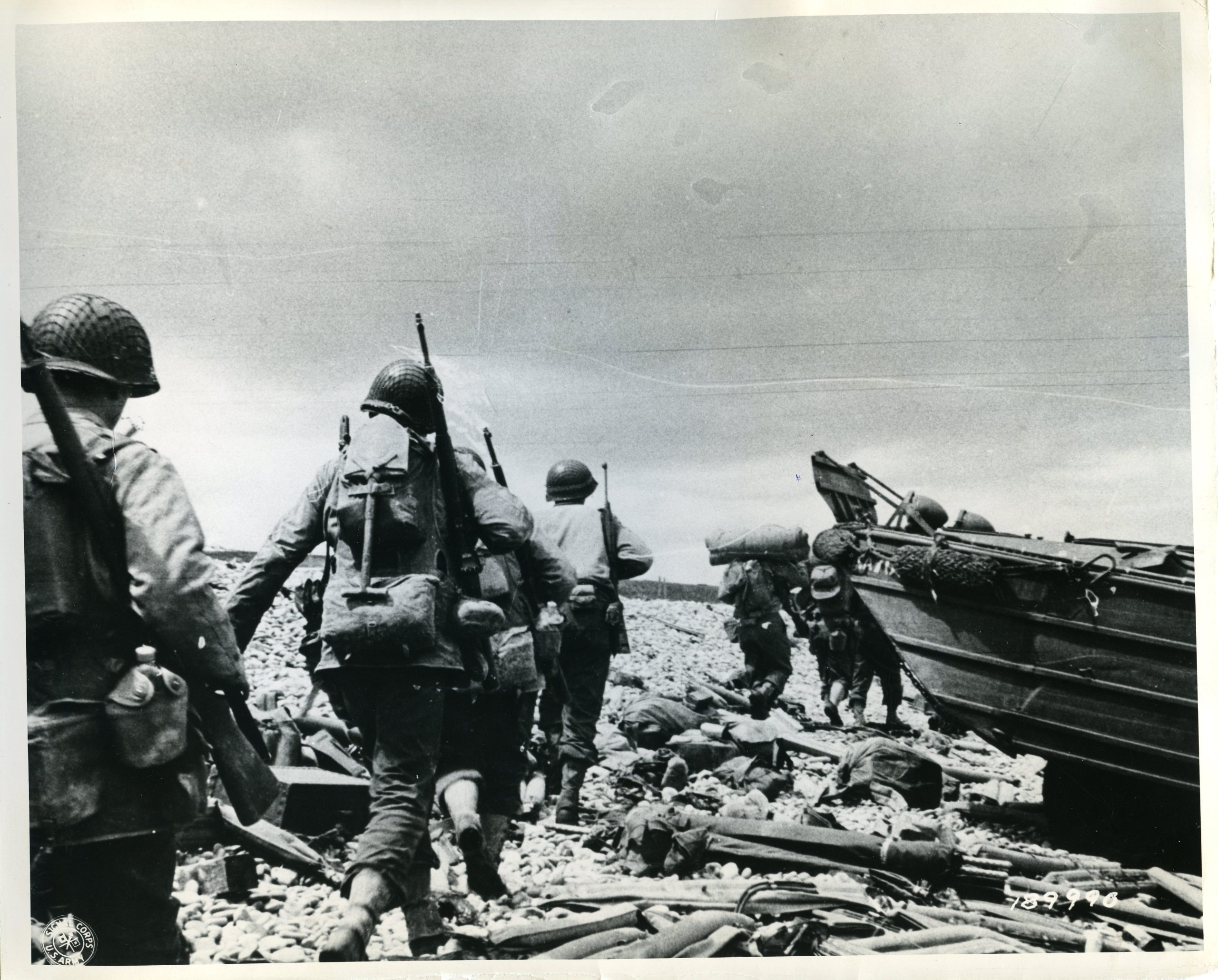 The original caption: "American assault troops move up the beachhead from their landing craft carrying... equipment, indicating their intent... make their visit a lasting one." Courtesy of National Archives.