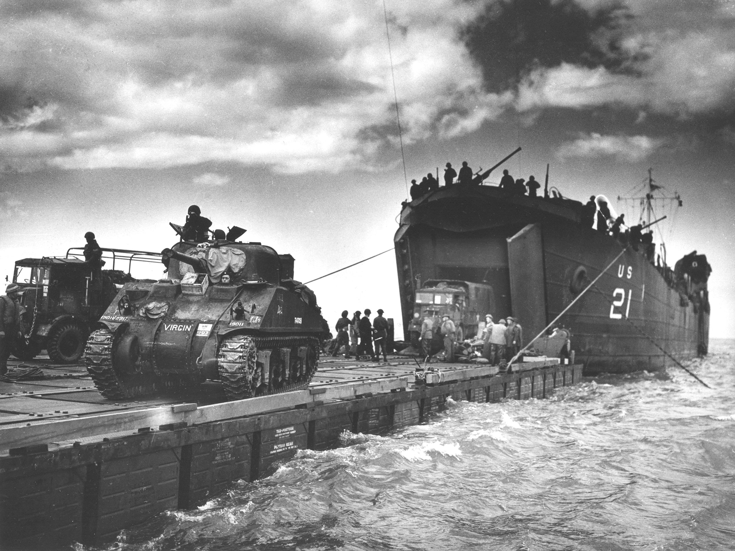 Without a deepwater port, constant supply and reinforcements were needed to break out of the beachhead. The solution was an artificial harbor built in England and brought to Normandy. Known by the codename “Mulberry,” two of these harbors were designed to unload men and supplies. Thousands of soldiers and sailors were involved in this effort. Spud barges that floated up and down with the tide formed the center of the harbor’s unloading activity. They were joined to the shore by floating roadways known as “Whales.” Courtesy of National Archives and National World War II Museum.