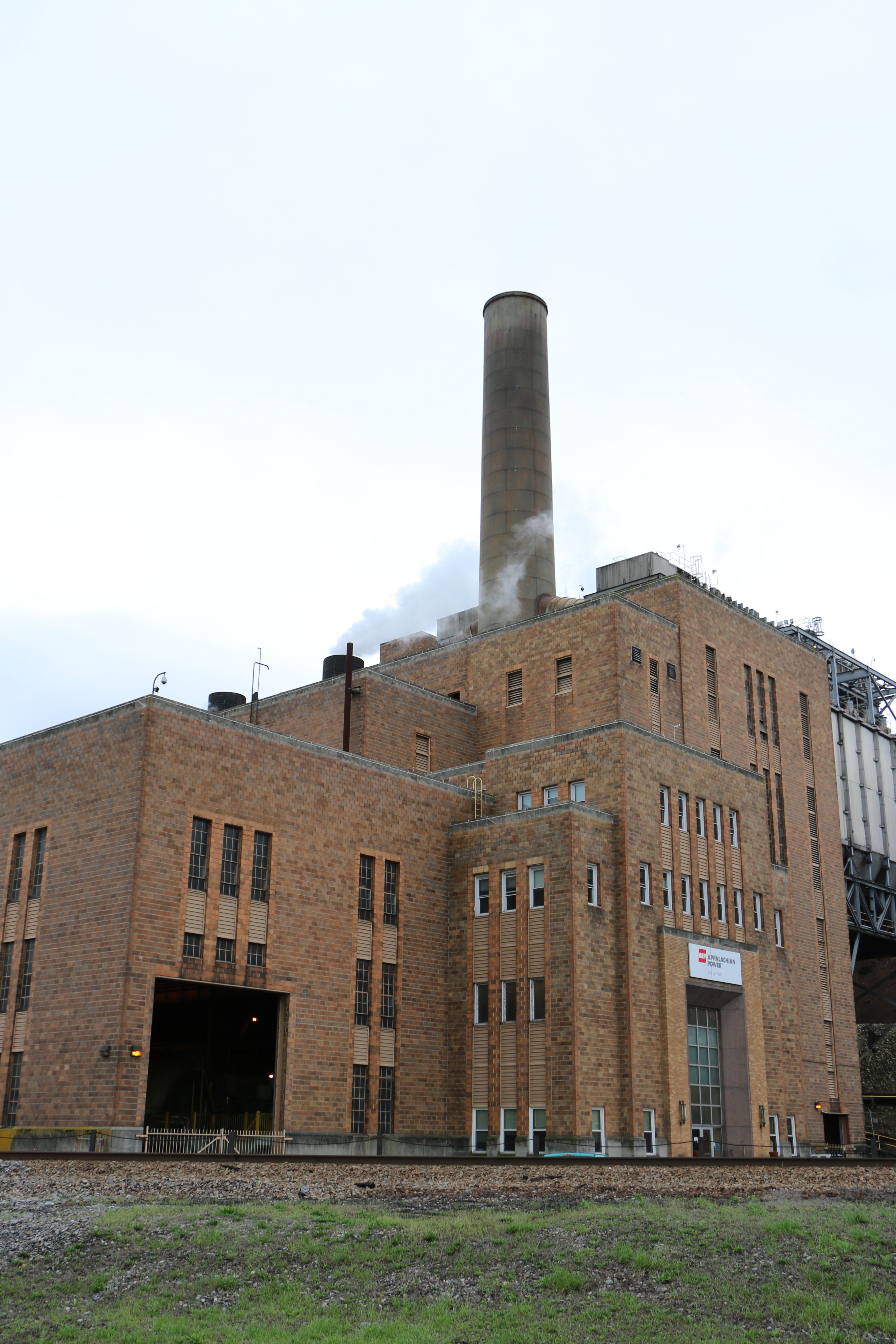 The front of an old brick power plant, with a smokestack rising from the center.
