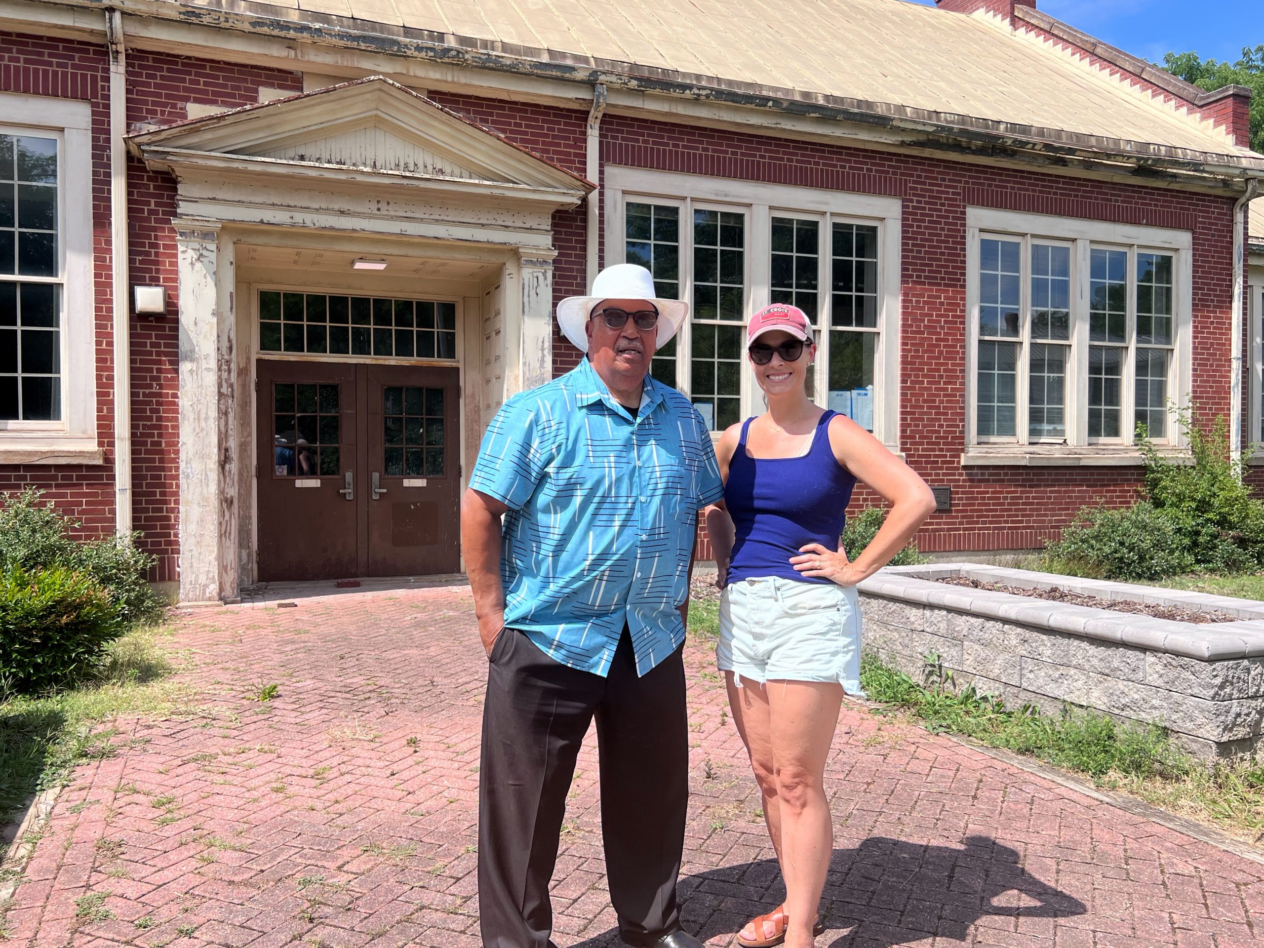 Mickey Hickman and Jill Williams stand in front of an old red brick school building.