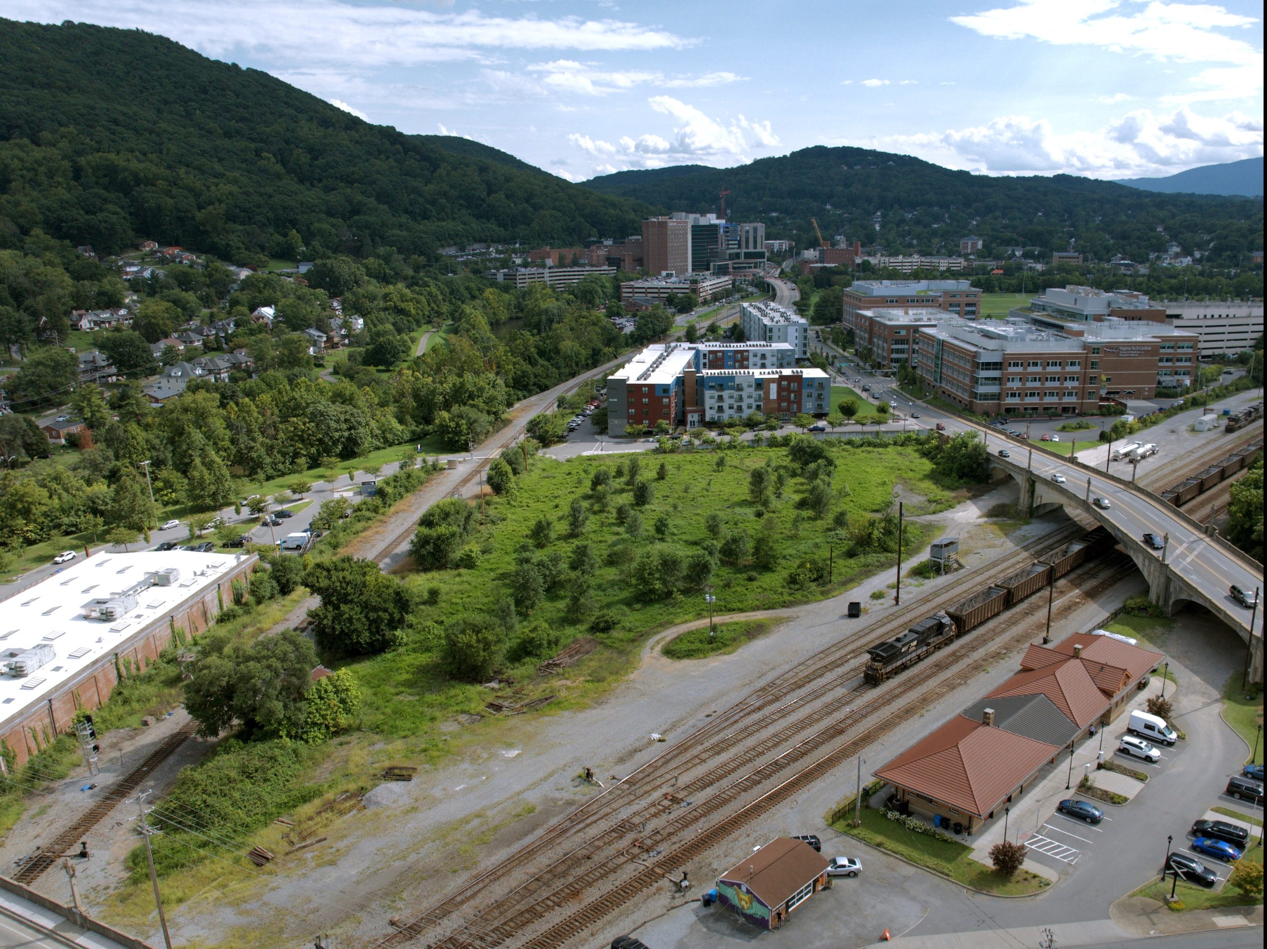 An aerial view of an area near the Riverside complex, with the railroad tracks in the foreground and a large empty green lot in the center.