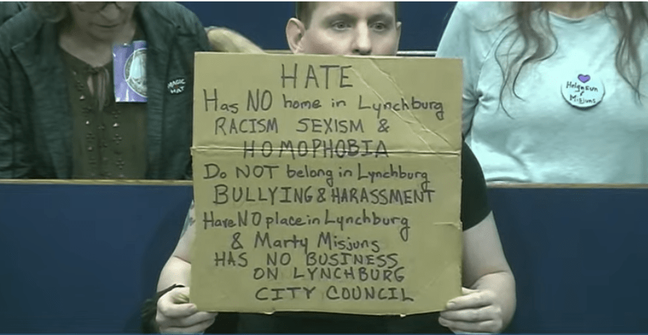 This person held up an anti-Misjuns sign throughout the meeting. In the row behind is someone wearing a pro-Helgeson and Misjuns button. Screenshot from livestream.