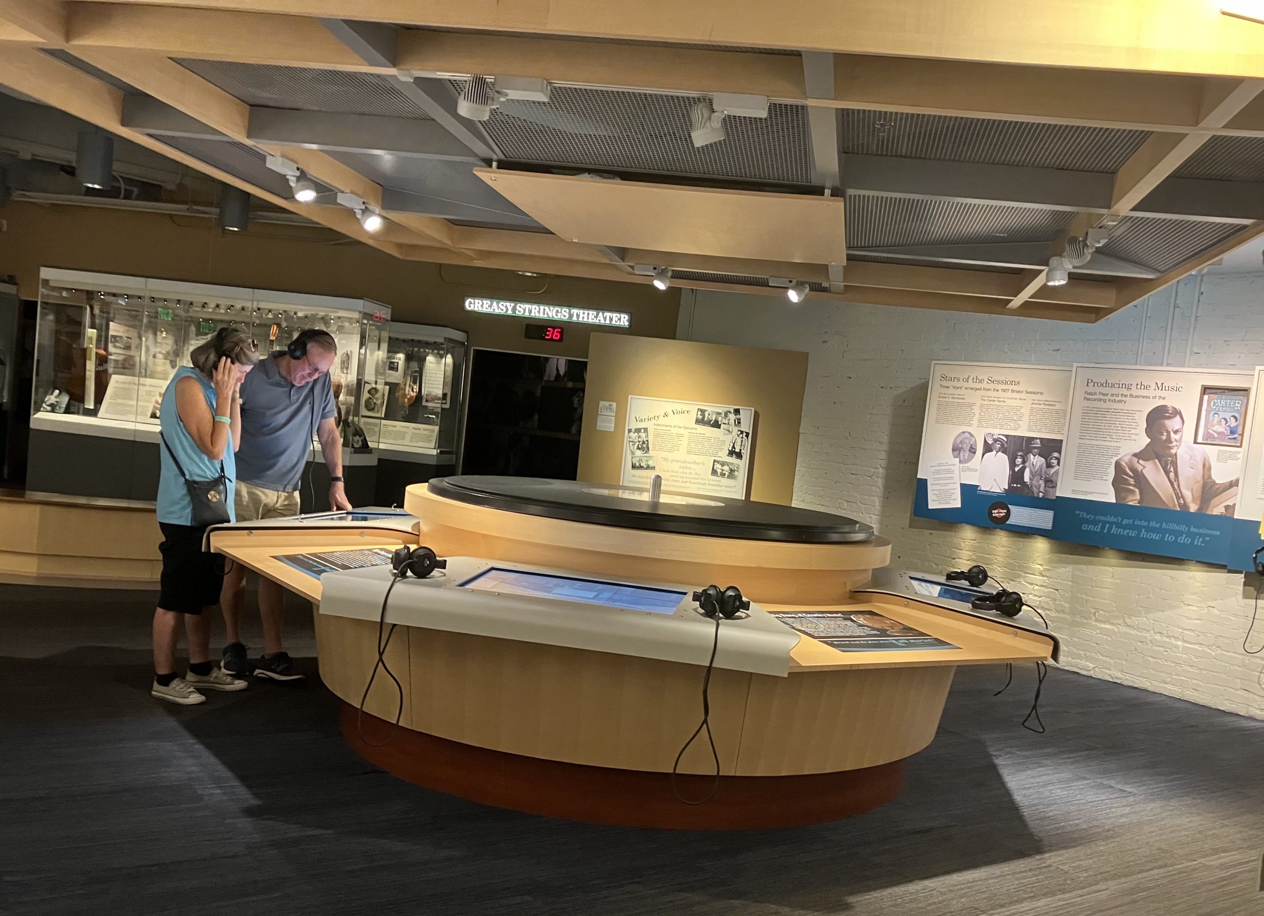 Two people stand in the middle of the Birthplace of Country Music Museum wearing headphones.