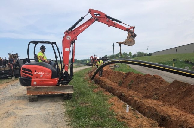 A worker digs with an excavator at a trench.