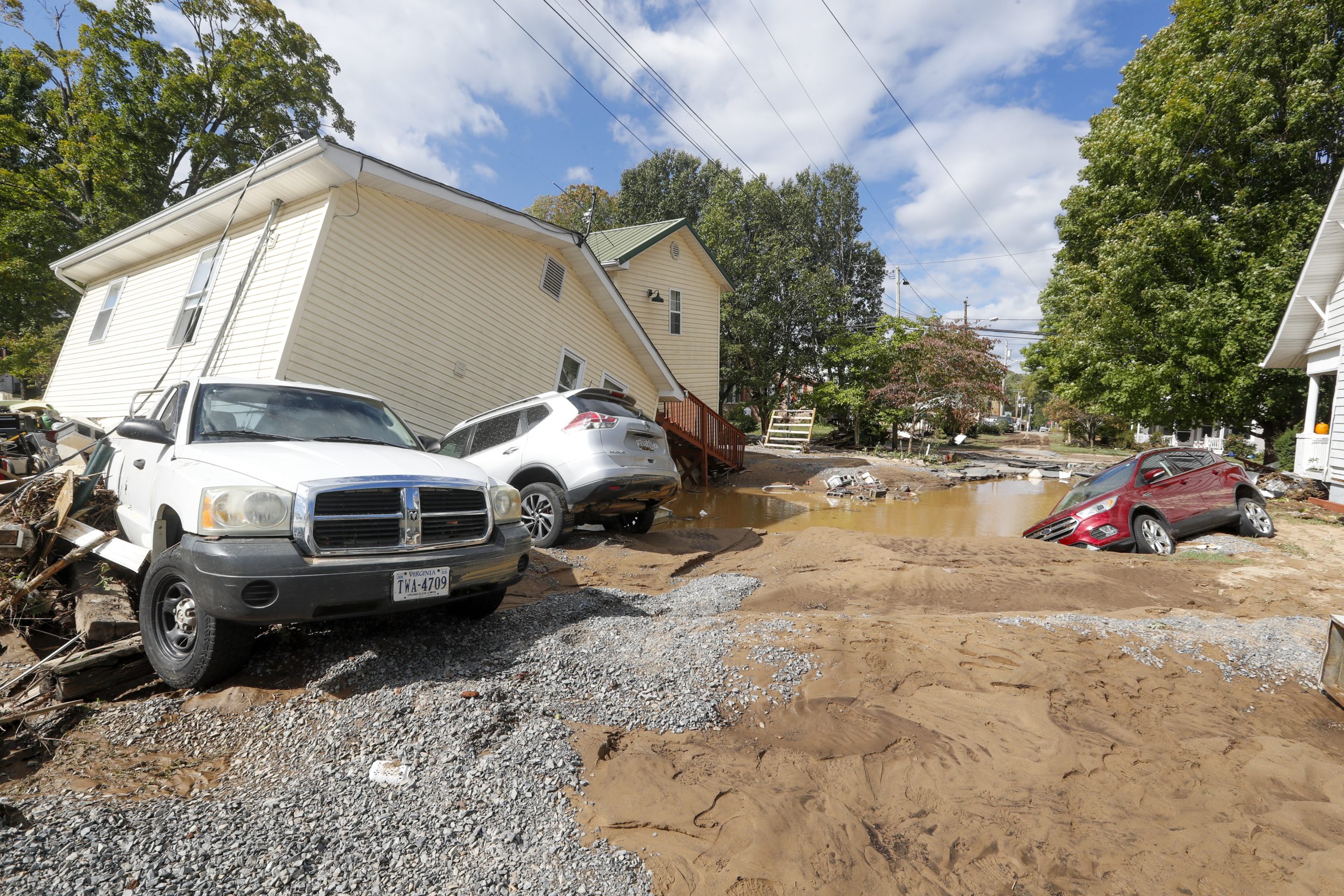 A single-story stick-built building knocked off its foundation, with several cars knocked around by floodwaters