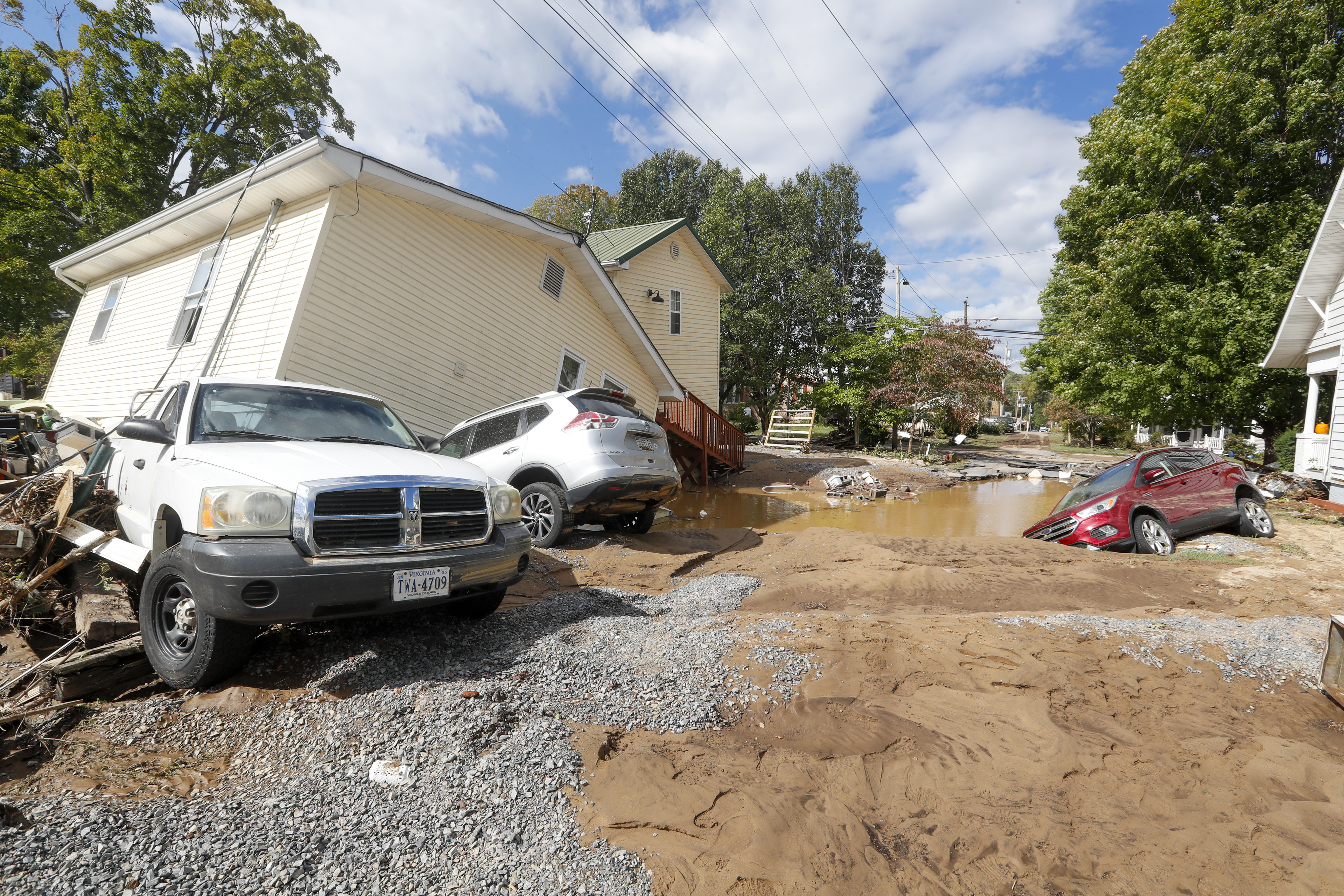 A single-story stick-built building knocked off its foundation, with several cars knocked around by floodwaters