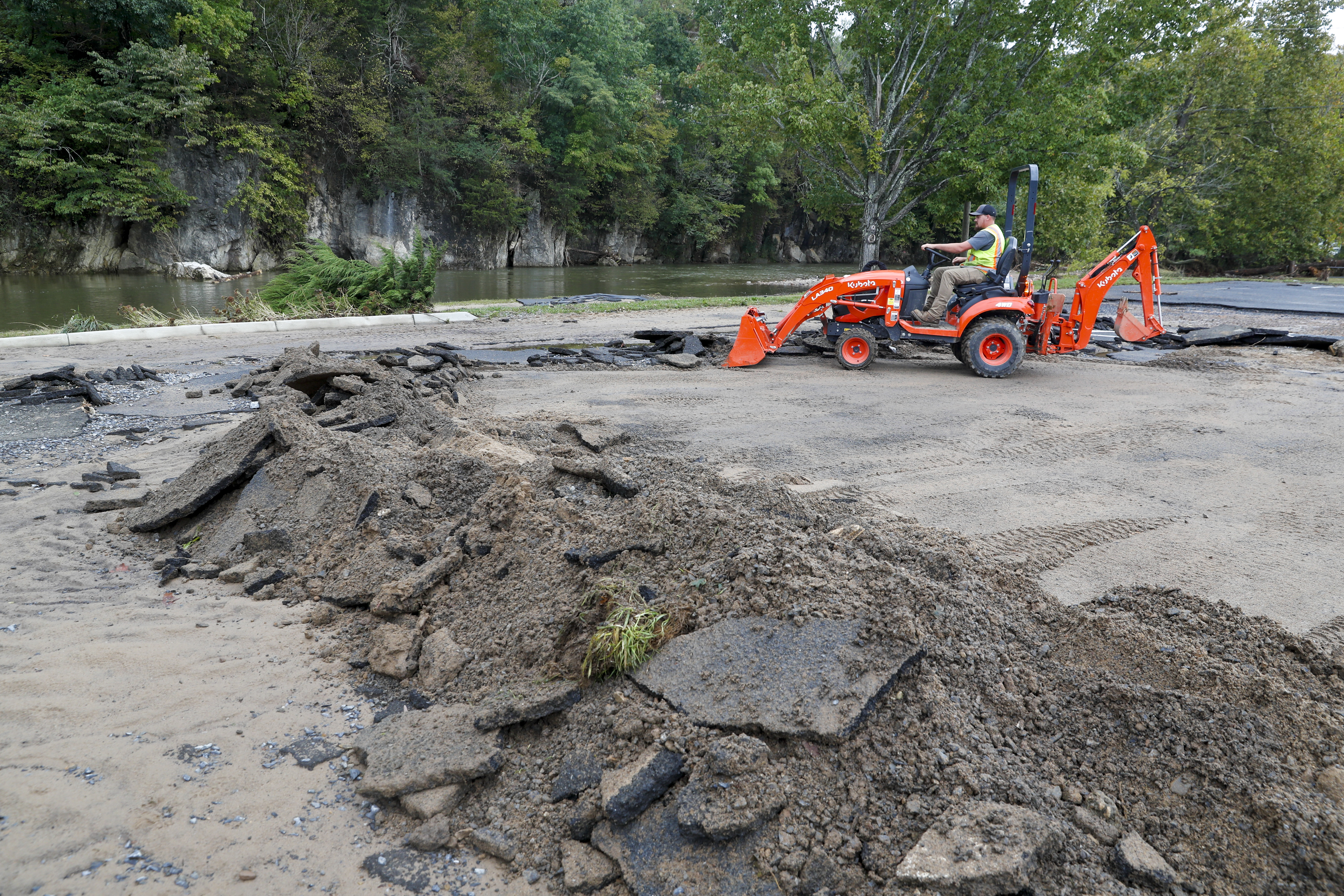 A man on a small skid loader cleans up debris in a park.