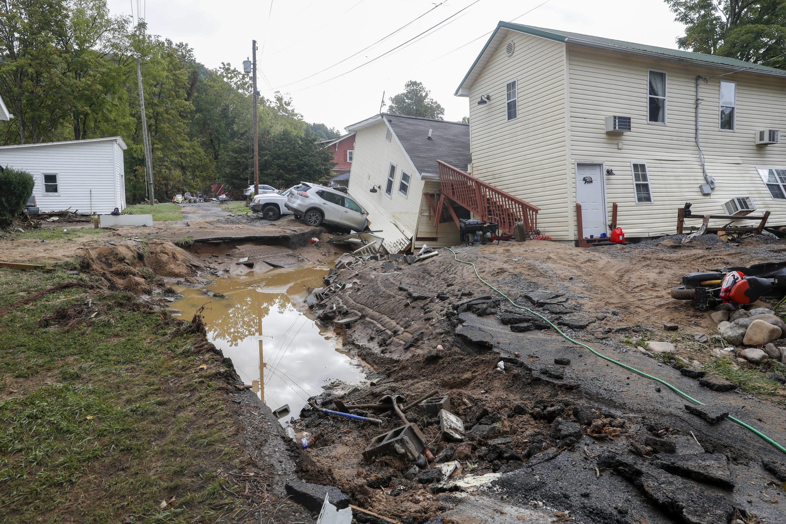 A small neighborhood of homes that have been knocked off their foundations, with cars run into them and muddy water in the foreground.