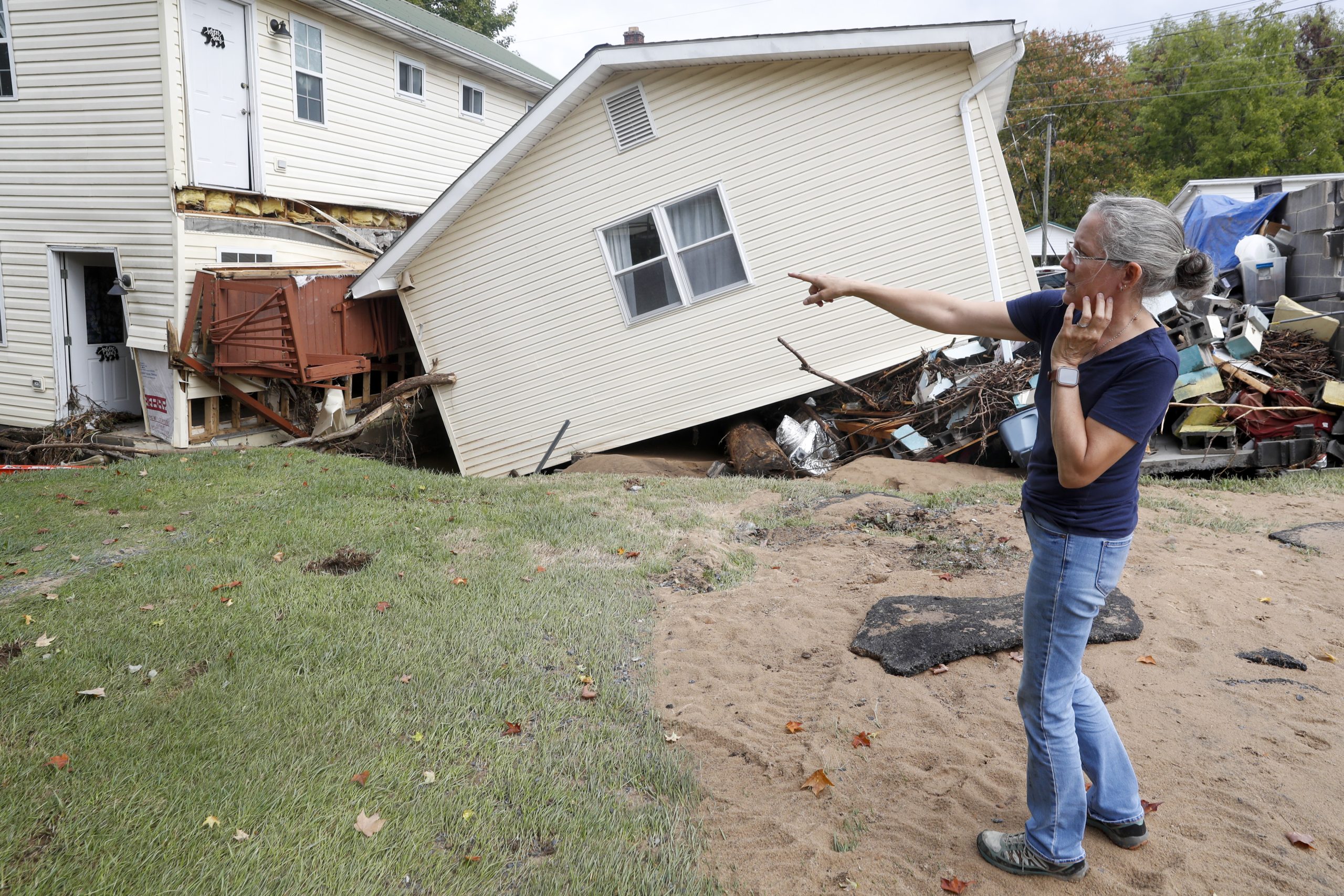 A woman points to a building that has been knocked off its foundation.