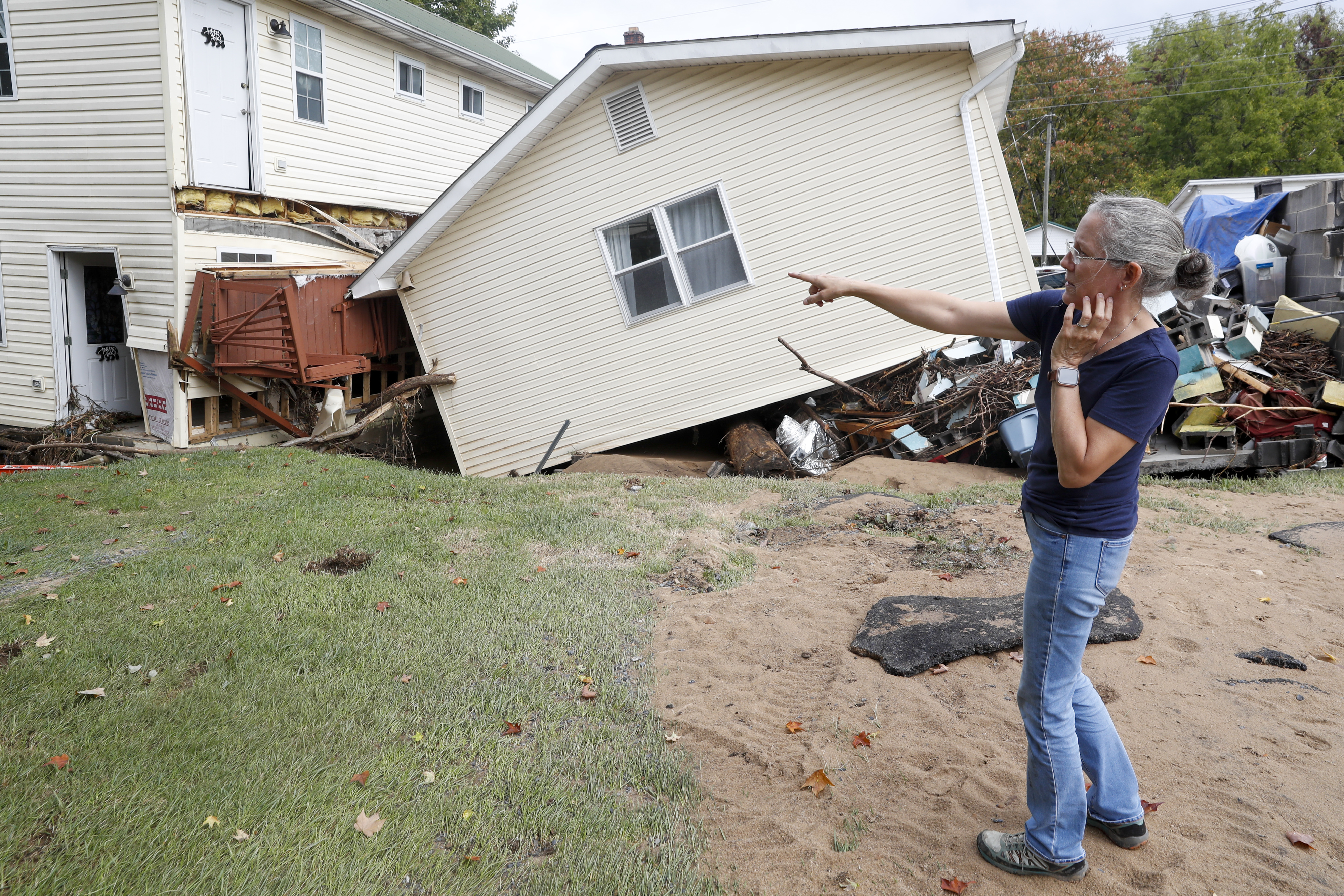 A woman points to a building that has been knocked off its foundation.