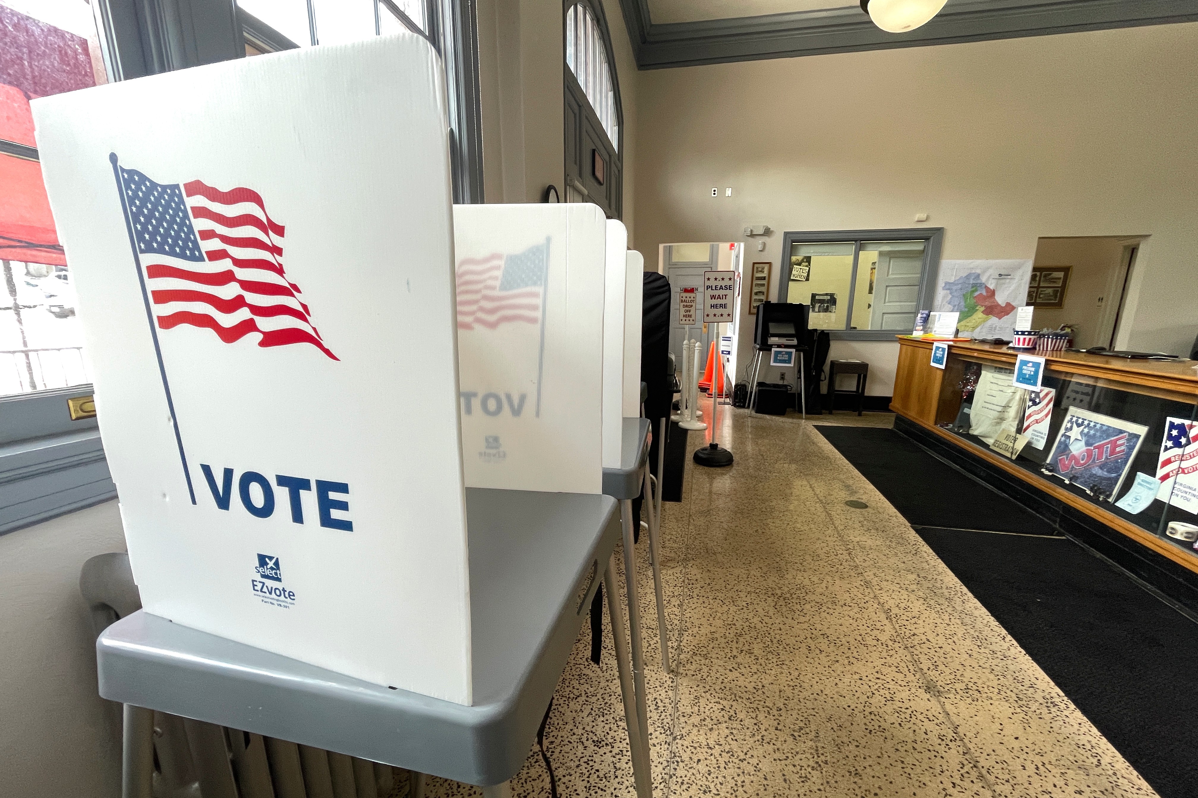 A line of voting booths with the word "vote" and a graphic of an American flag are inside an office.