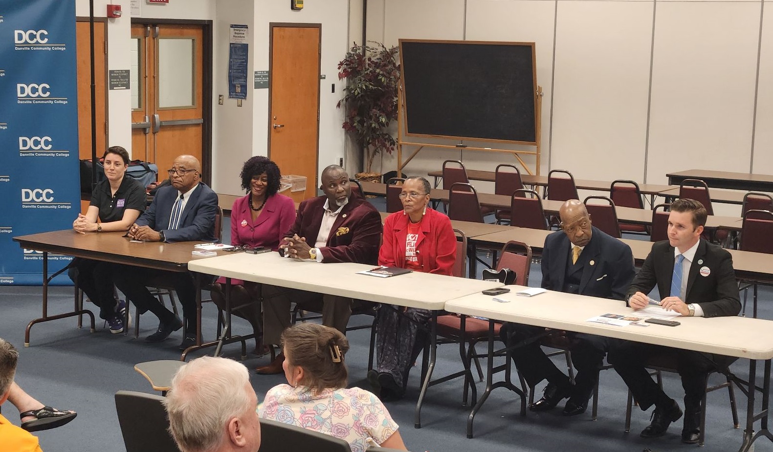 Danville City Council candidates (from left) Maureen Belko, Lawrence Campbell Jr., Petrina Carter, Barry Mayo, Felice McWilliams, Sherman Saunders and Lee Vogler sit at a long table in the front of an auditorium