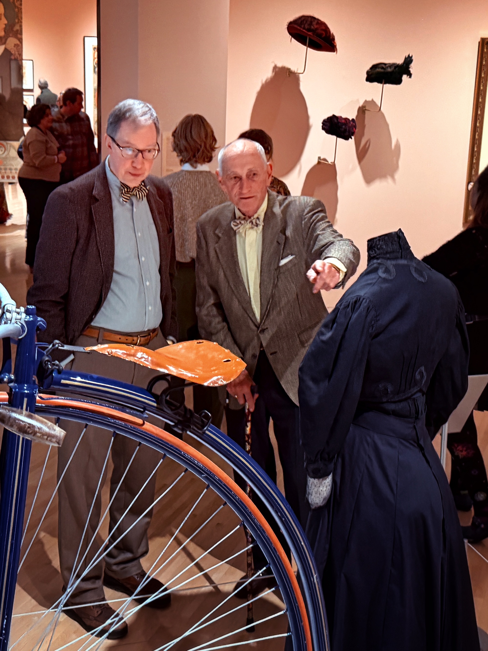 Two men look at a bicycle over a hundred years old at a museum exhibit.