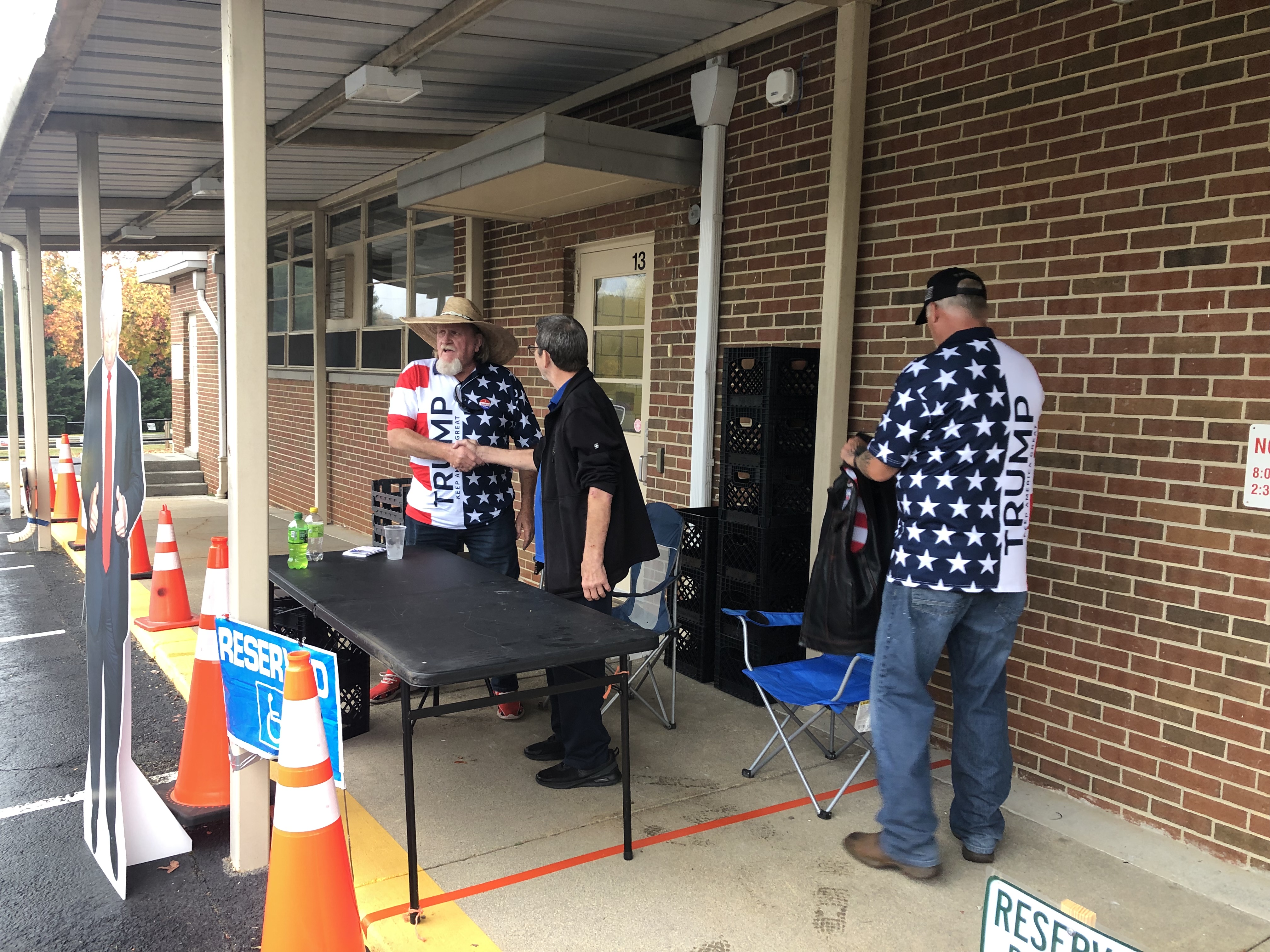Boones Mill mayoral candidate Donald "Whitey" Taylor stands center left in front of Boones Mill Elementary School, greeting a supporter from behind a table on the school sidewalk.