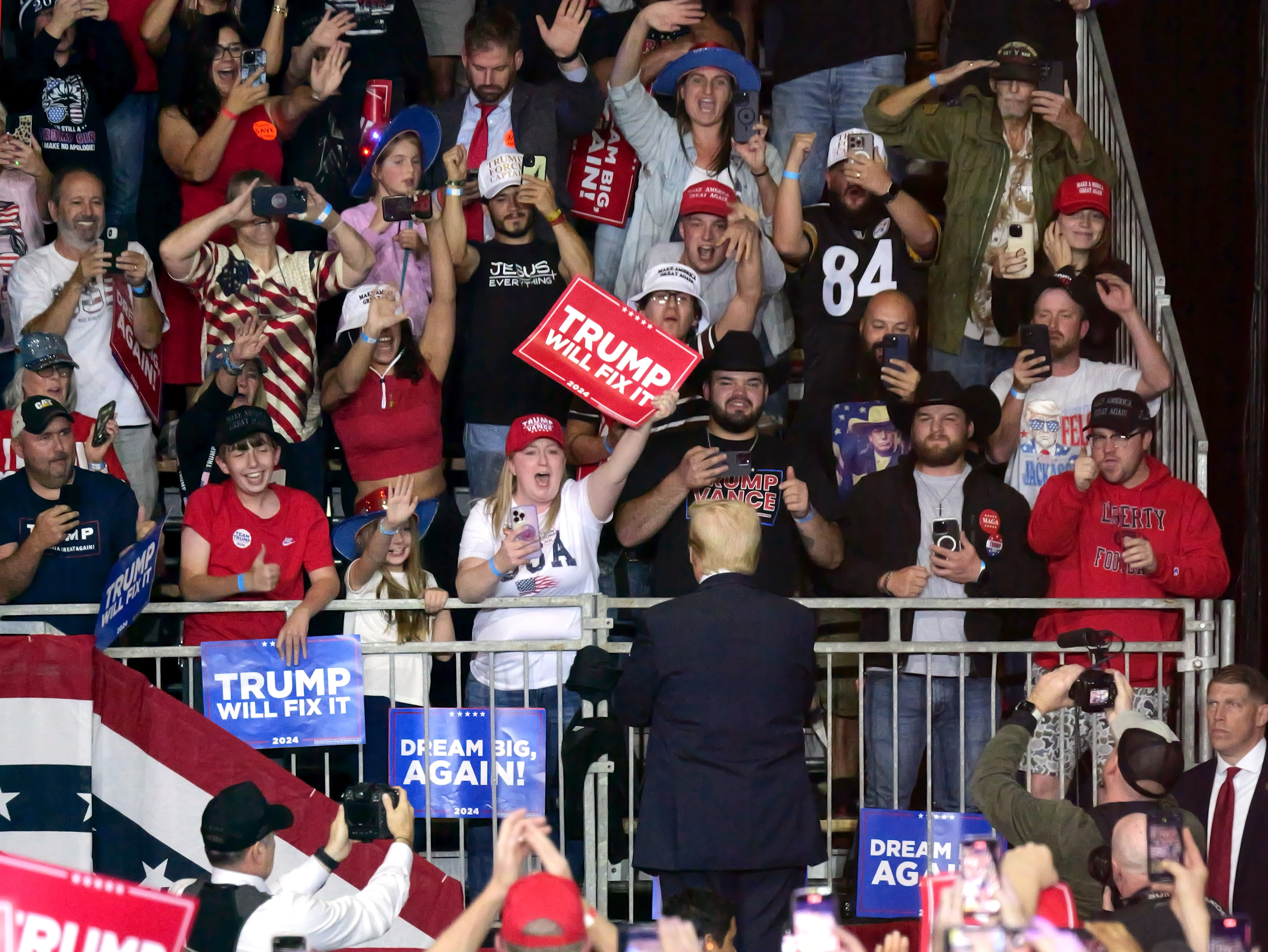 Former president Donald Trump stands on a stage, facing the crowd behind the podium and acknowledging their support.