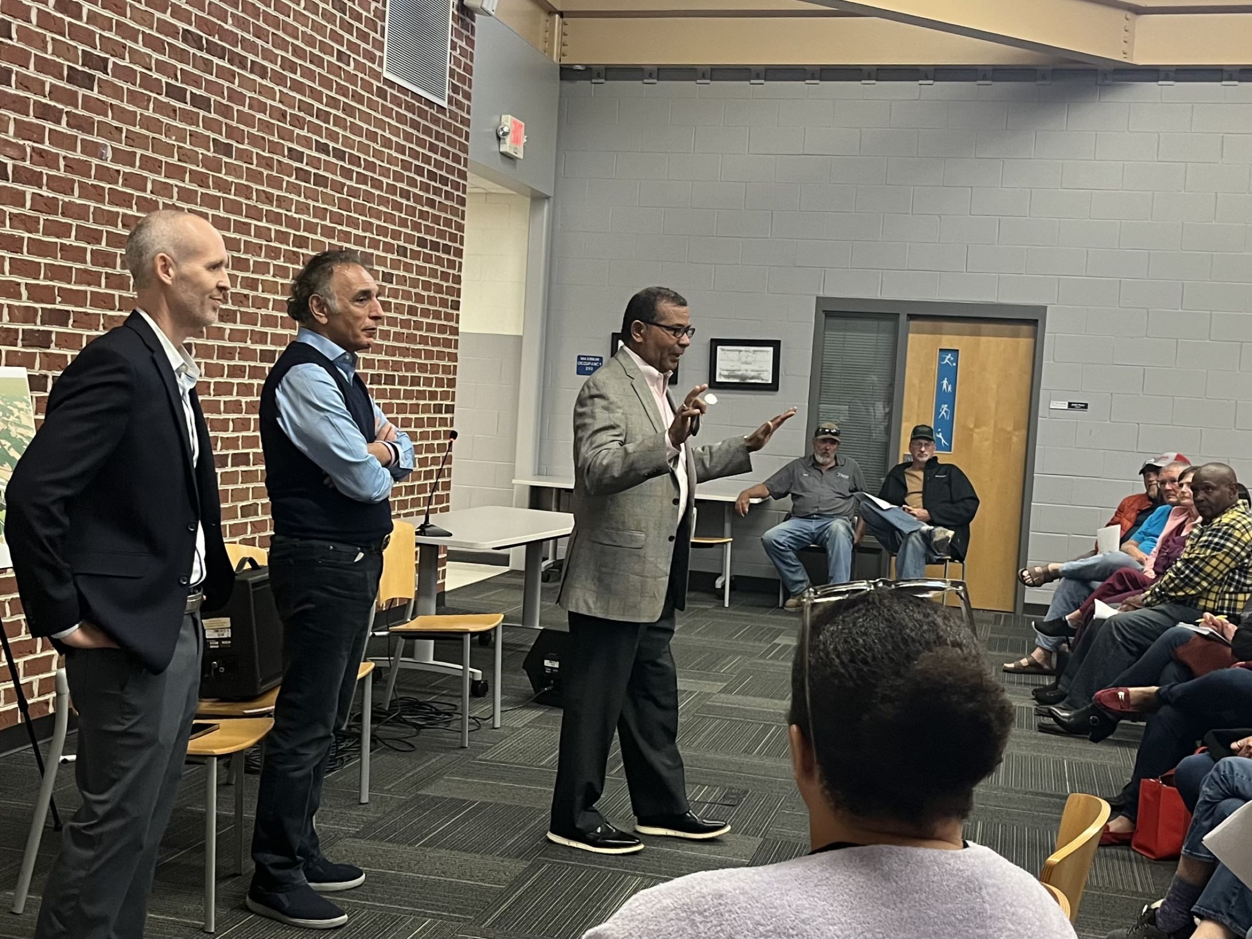 Three men, Tim Hope and Irfan Ali of Balico, and Robert Tucker, county supervisor, stand in front of a crowd at a community meeting in Chatham.