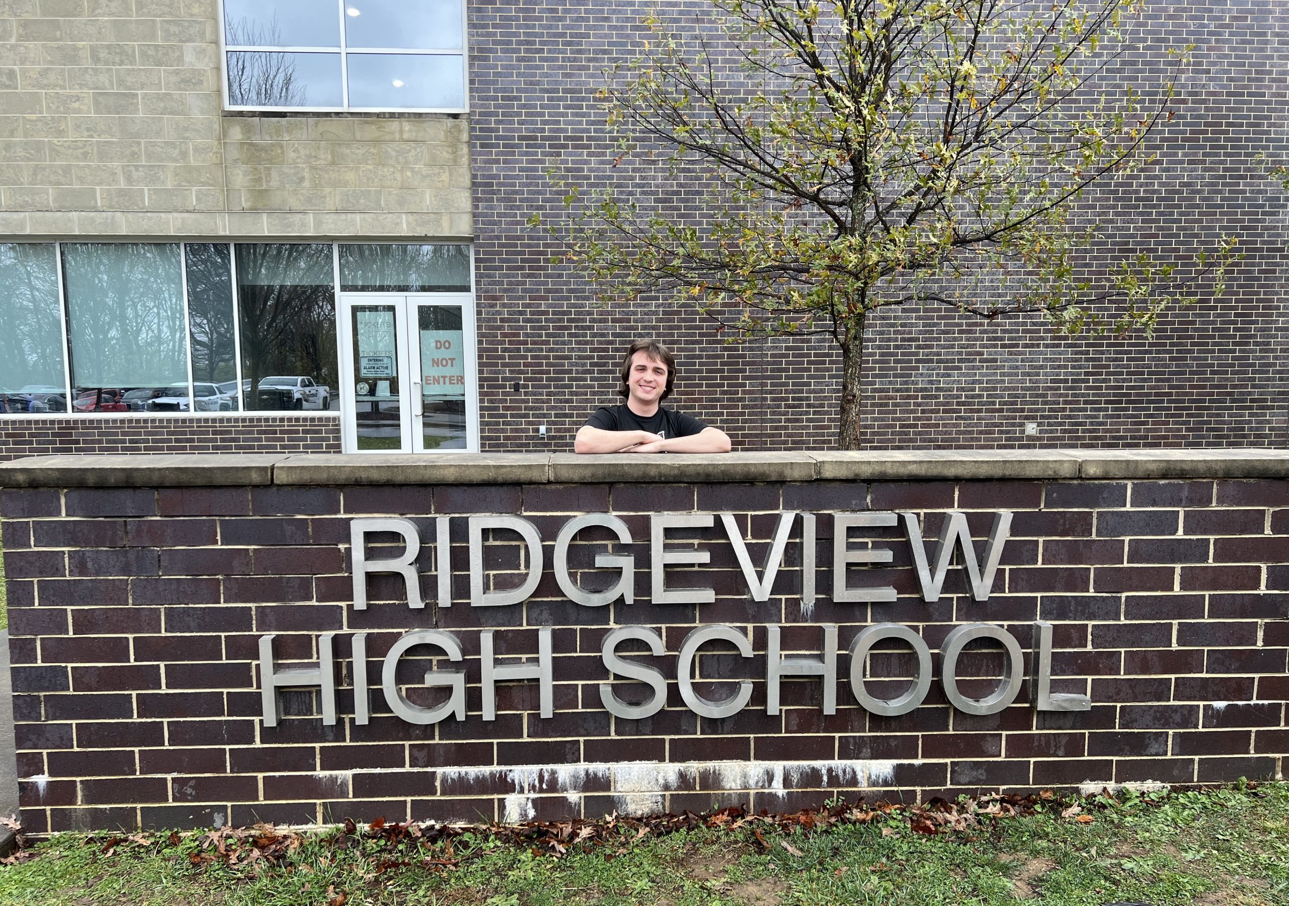 Daniel Greear, a high school student, stands behind a sign reading "Ridgeview High School"