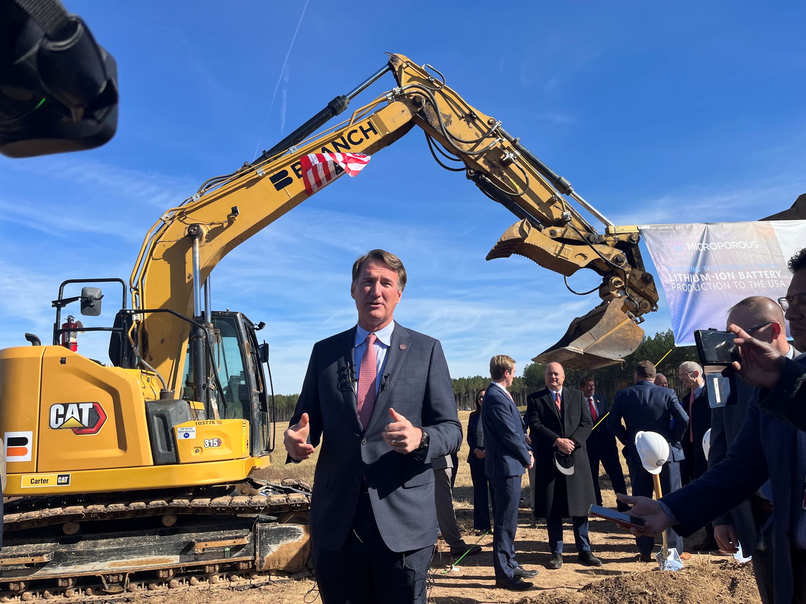 A man, Virginia Gov. Glenn Youngkin, stands framed by bulldozers at the Southern Virginia Megasite at Berry Hill.