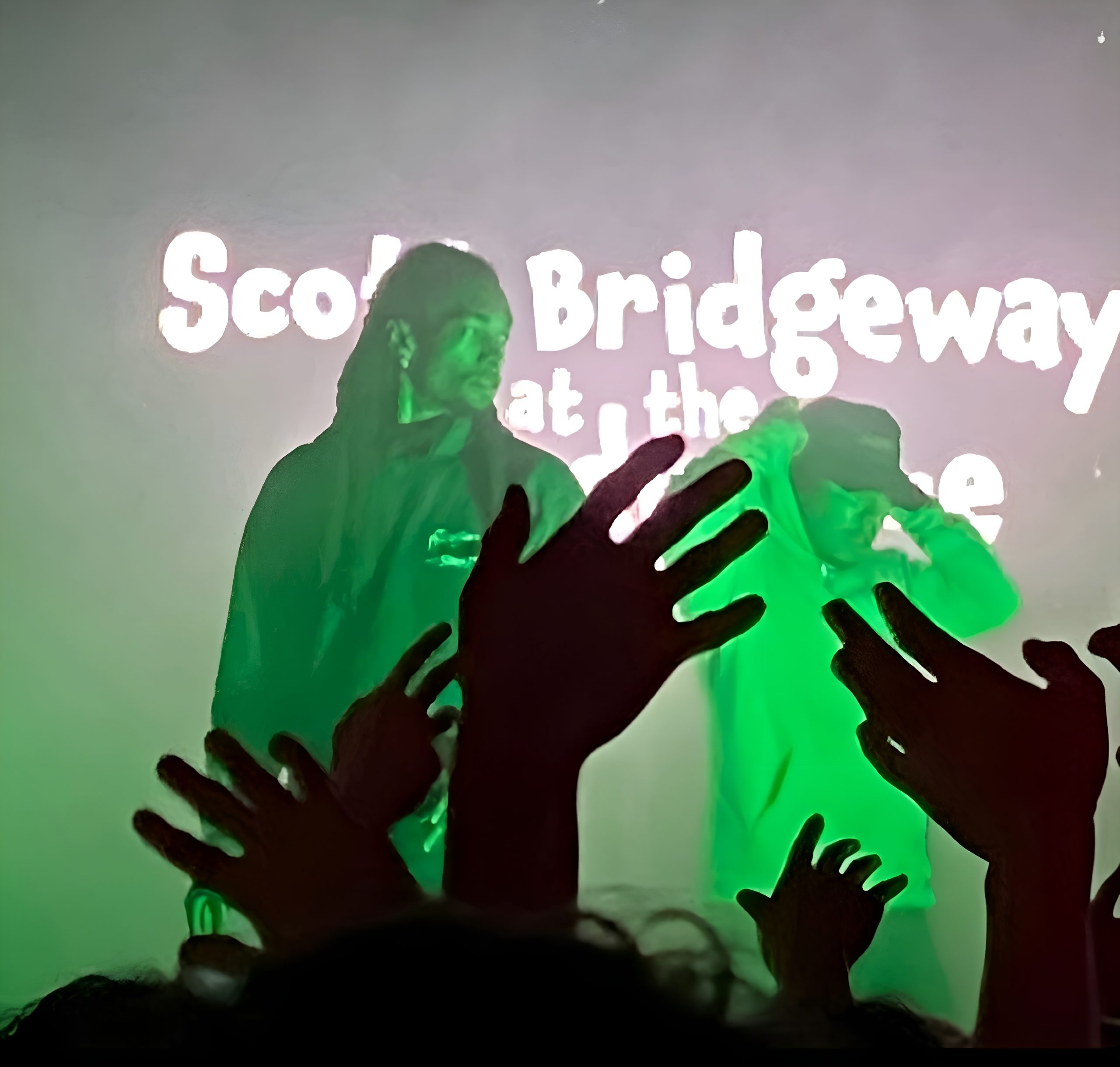 Ruchaun Akers lit by a green light stands in front of a screen that says "scott bridgeway"