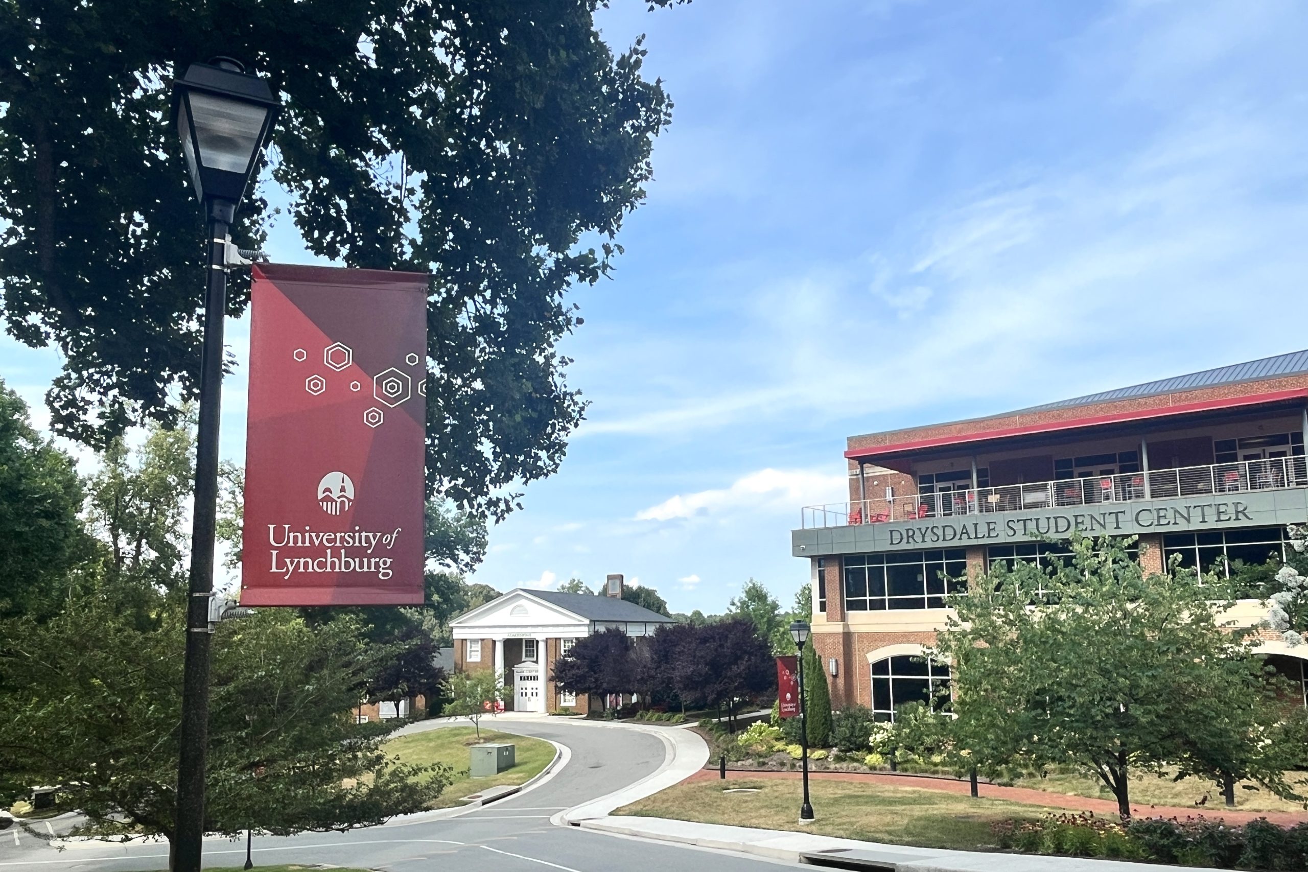 A view of the University of Lynchburg campus including a banner on a light post, the admissions building, and the Drysdale Student Center.