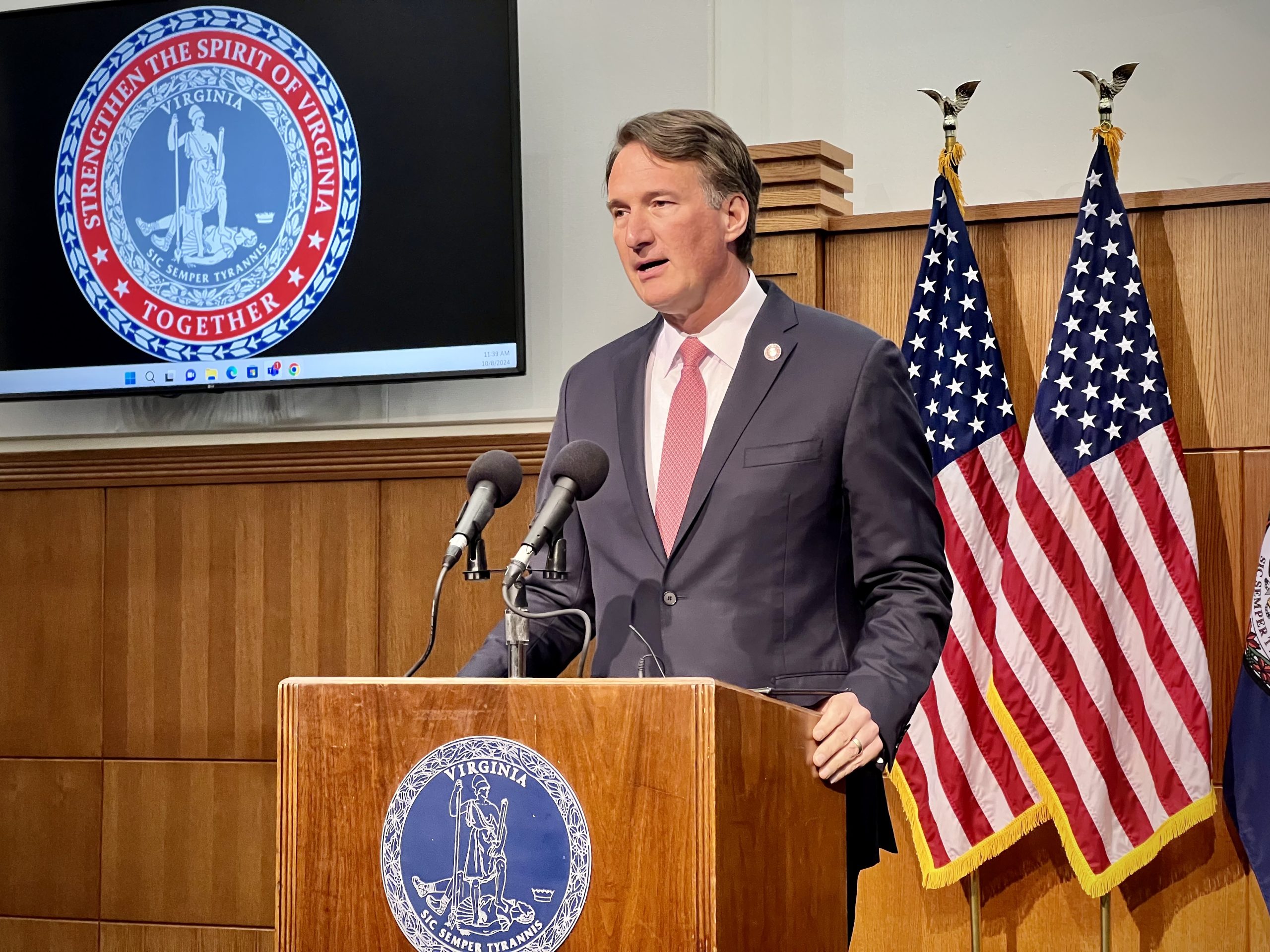 Gov. Glenn Youngkin stands at a brown lectern with american flags behind him.