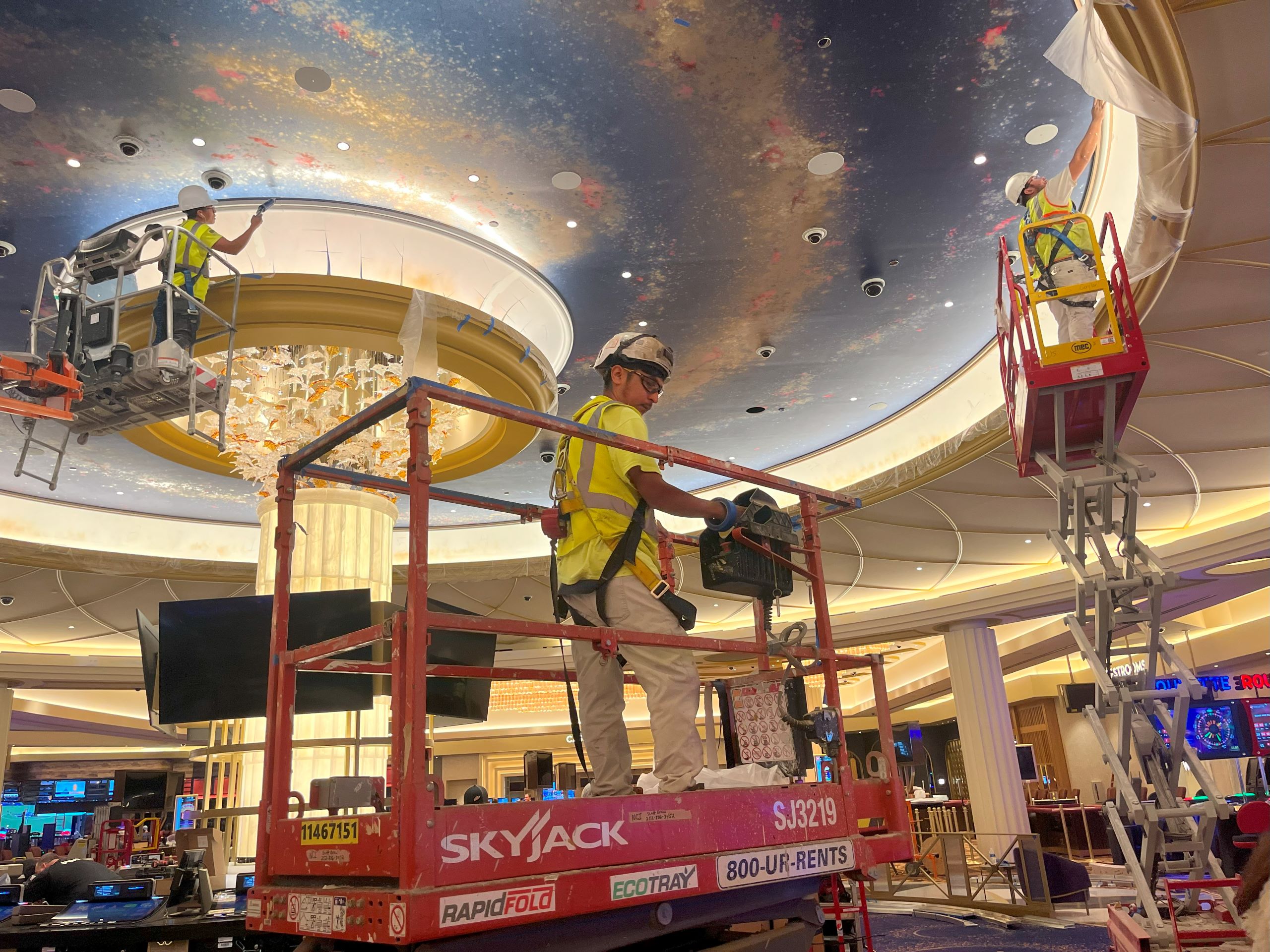 three construction employees on lifts work on the ornate ceiling of the gaming floor in the Caesars Virginia casino resort.