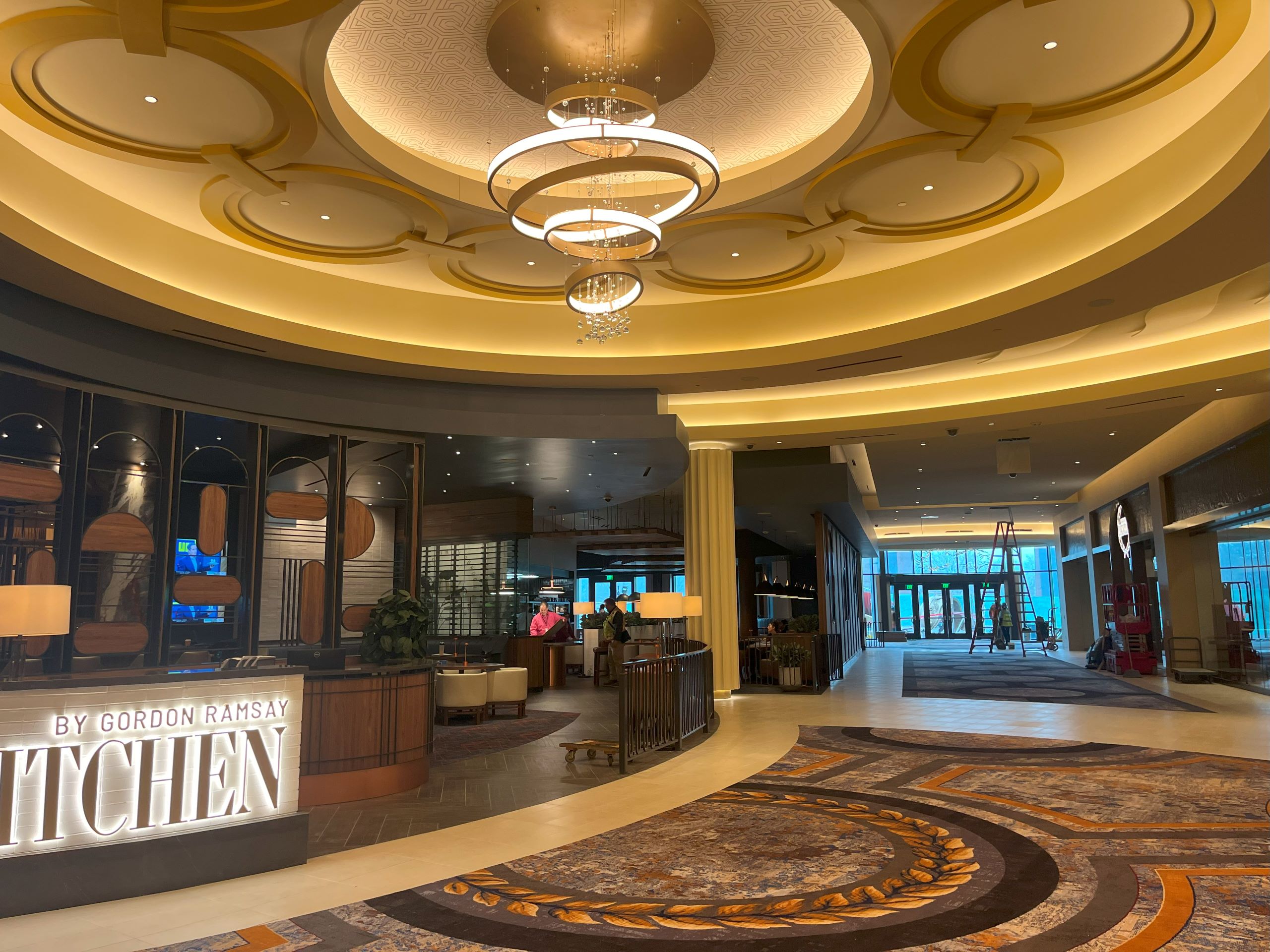 a chandelier hangs over a golden and white lobby space in the casino resort.