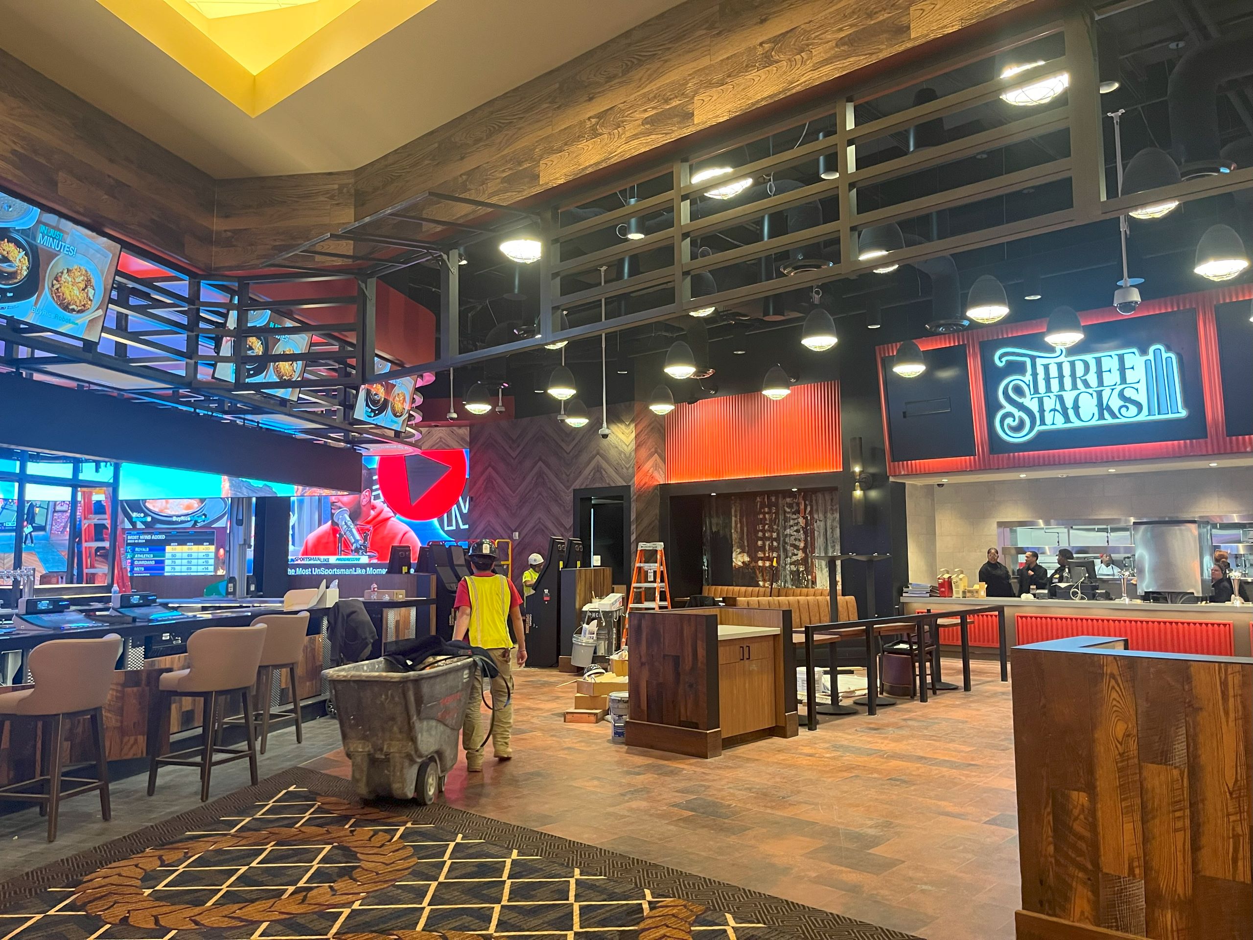 An employee in a bright yellow vest wheels a container through a bar area in the casino resort.