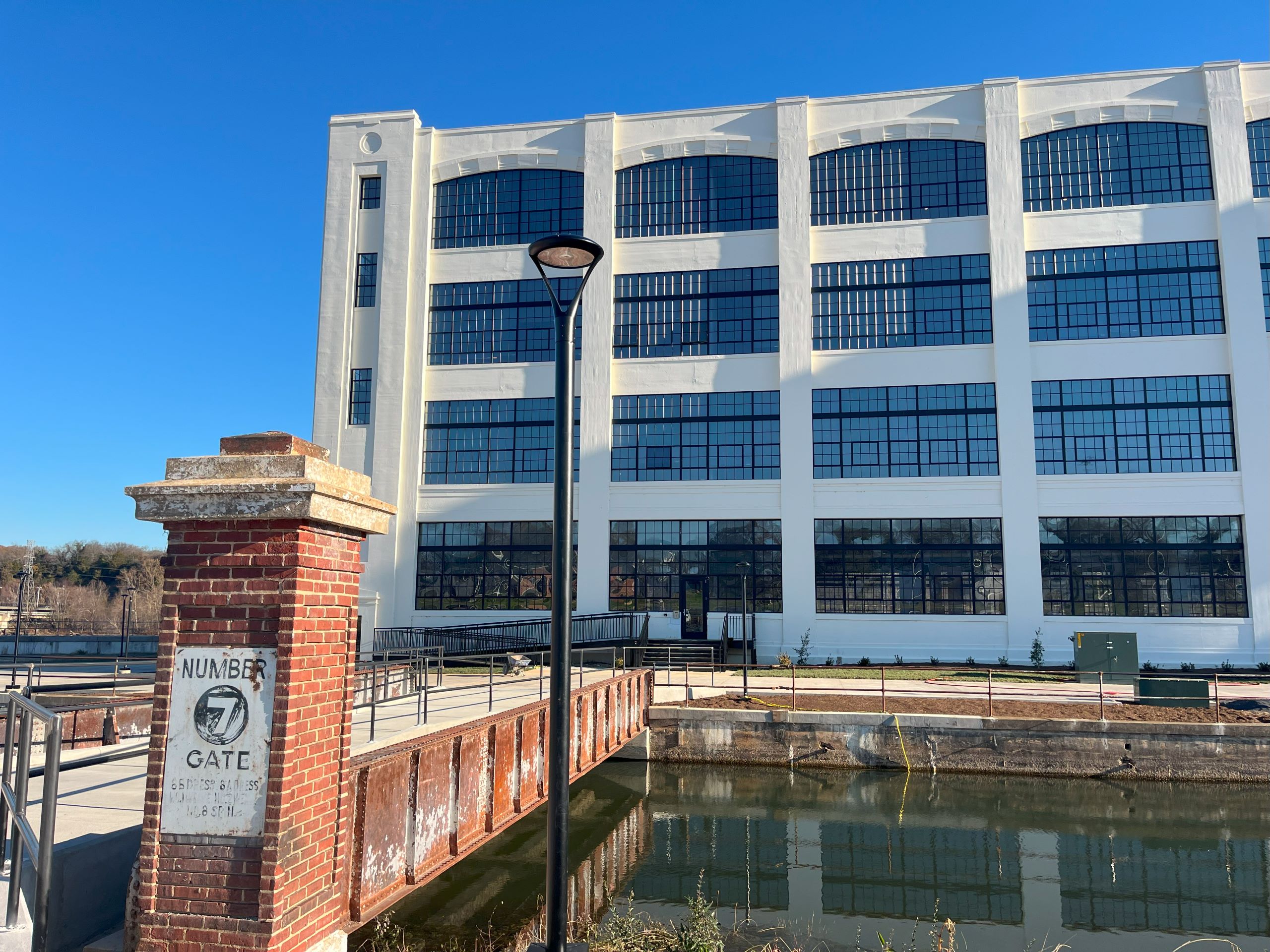 A brick column stands in front of a metal bridge outside a refurbished mill building in Danville, with large windows. The sign on the column reads "Number 7 gate."