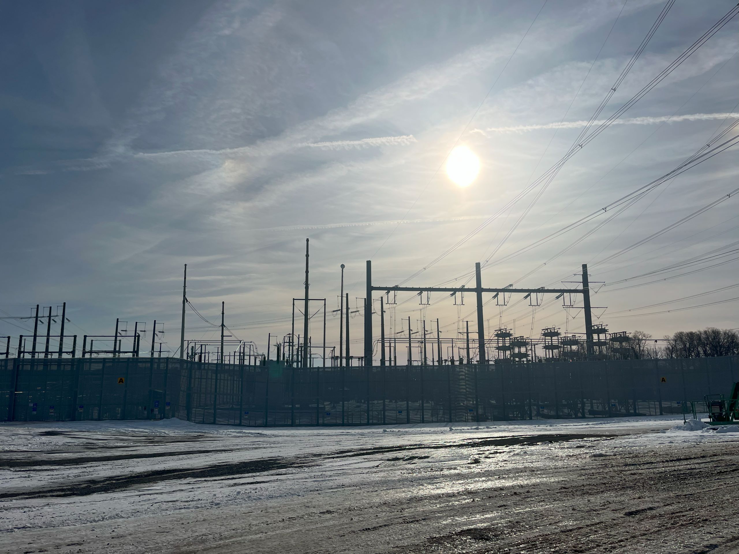 the sun shines above a substation in Northern Virginia. It's transmission lines and infrastructure is silhouetted against the sky
