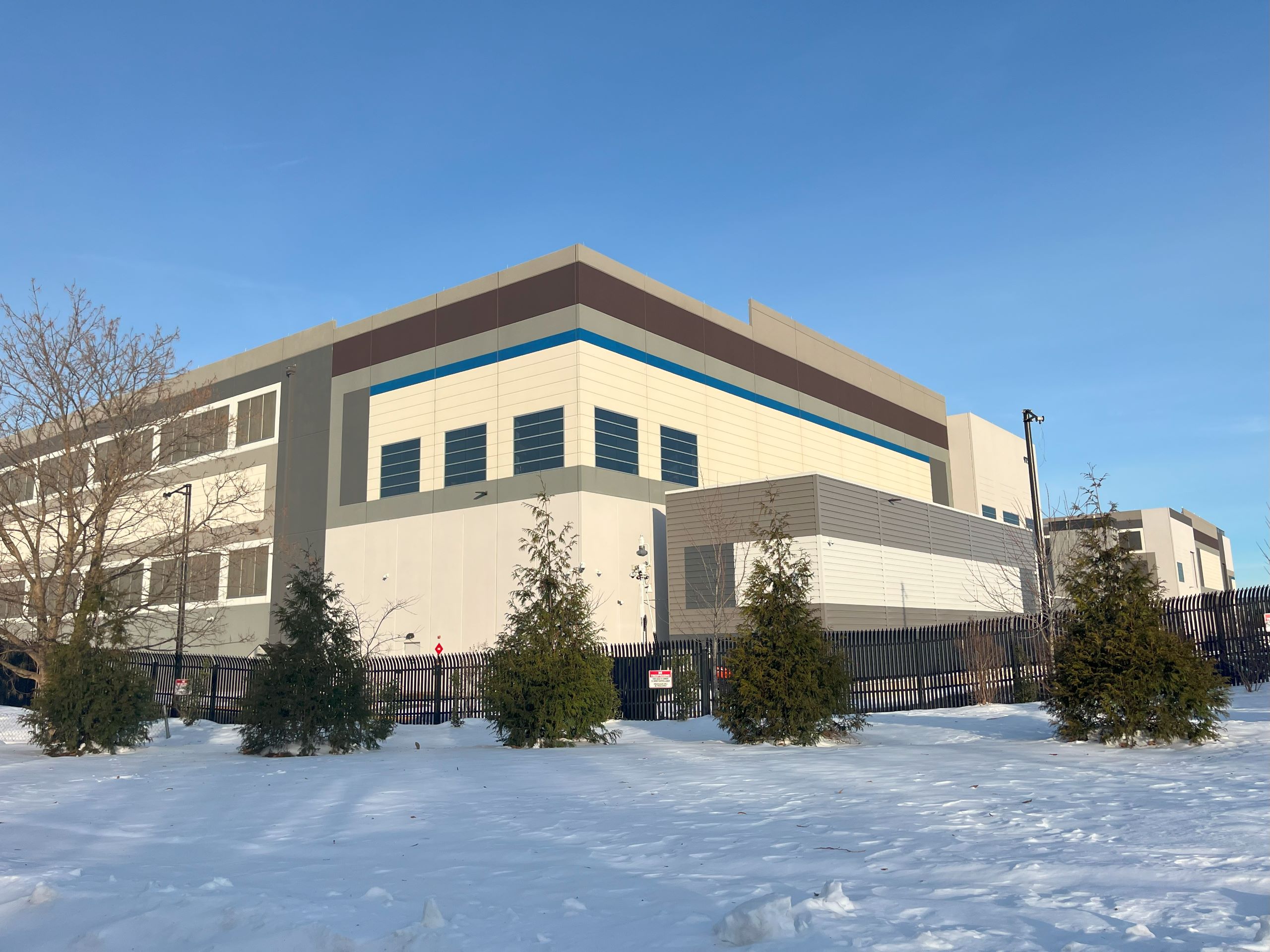A large building with a fence and small trees surrounding it, the Amazon Tanner Way data center in Prince William County
