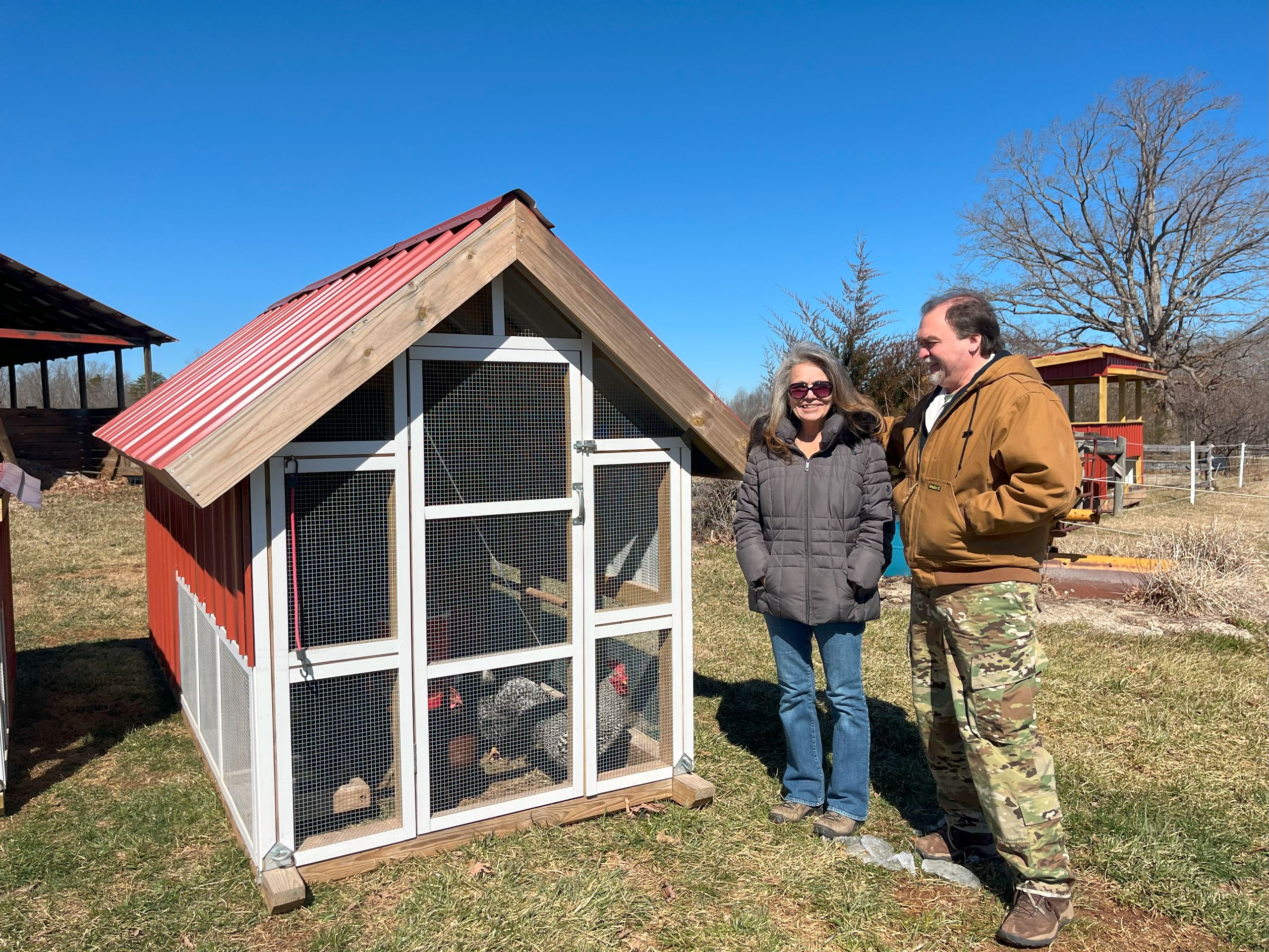 a couple stands in front of a chicken coop outside their Pittsylvania County home