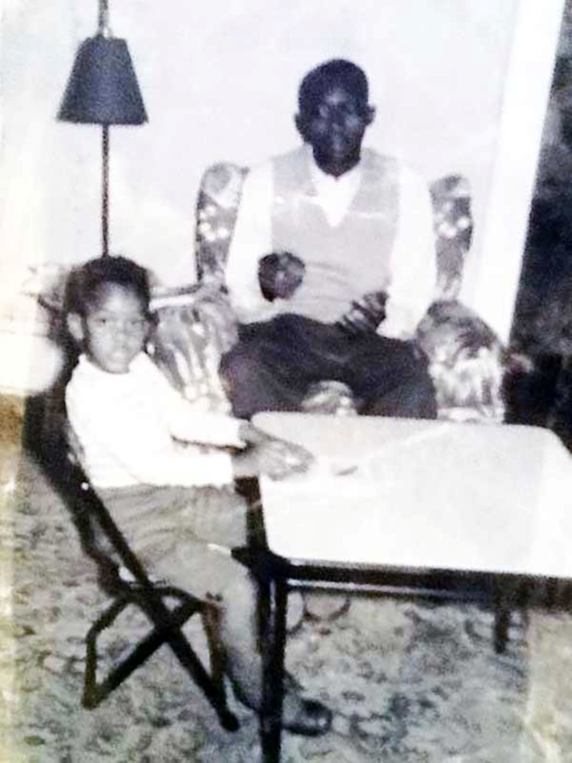 a black and white photo of a young girl, Andrea Burney, sitting at a table with her father, George Burney