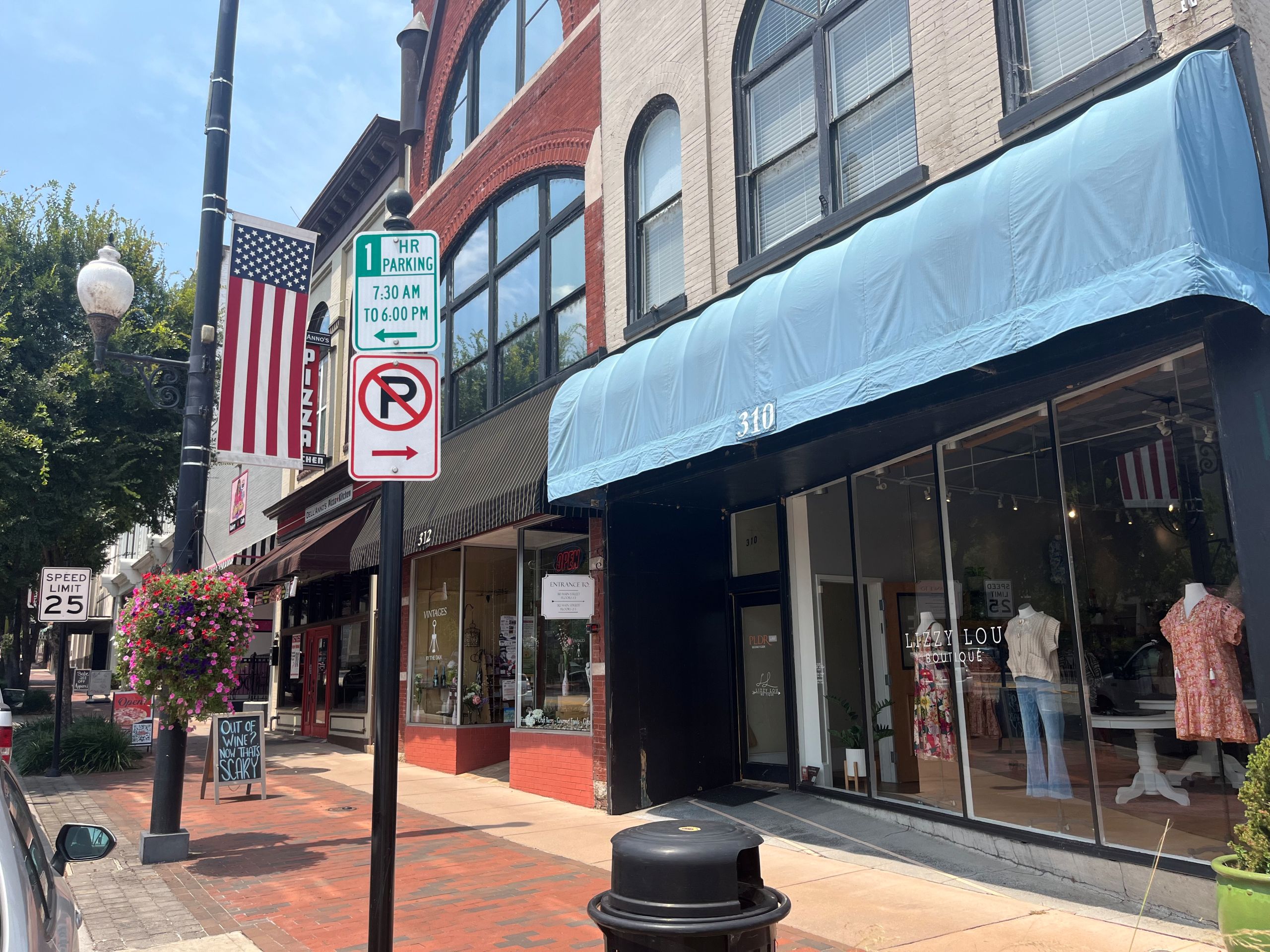 a sidewalk of Danville's Main Street, with a strip of retailers behind a sign that reads "1 hour parking"