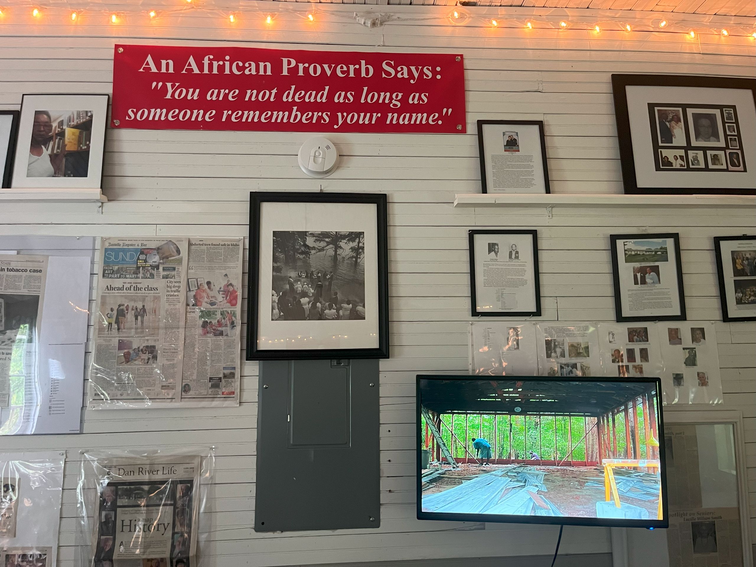 a white paneled wall is decorated with framed photos, quotes, and newspaper clippings. This is the inside of the Harvey School