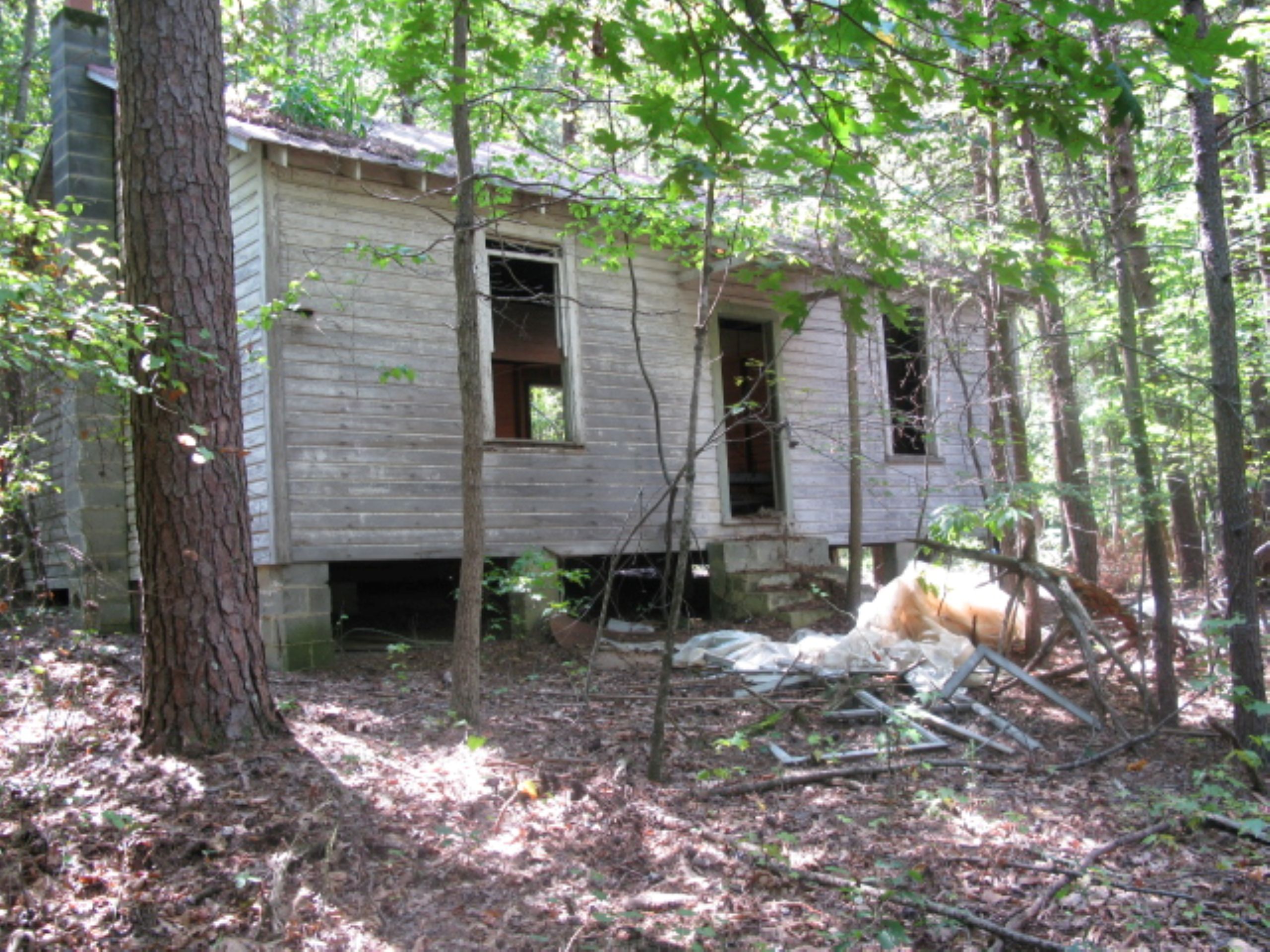 an old wooden schoolhouse without doors and windows sits on cinderblock stilts in the woods. This is the Harvey Schoolhouse