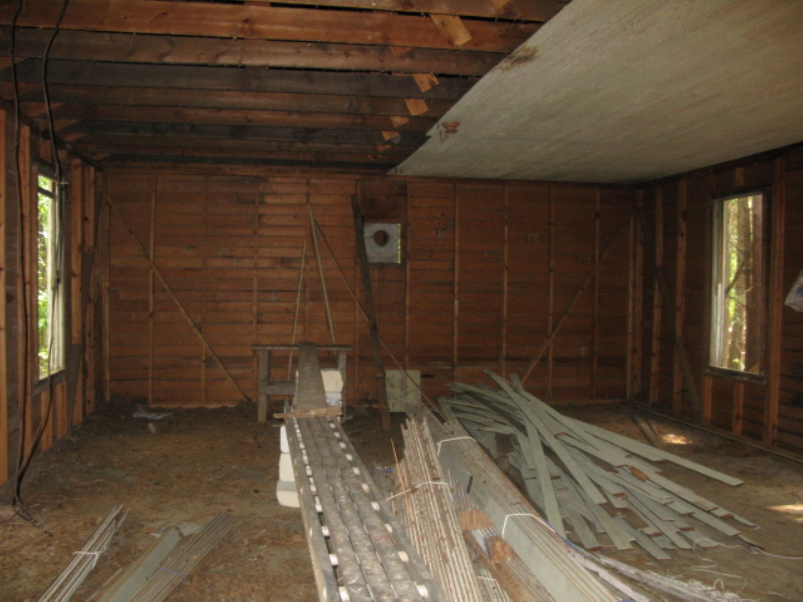 inside a one-room schoolhouse, pieces of wood forming the ceiling have been partially dismantled and lay in piles on the floor