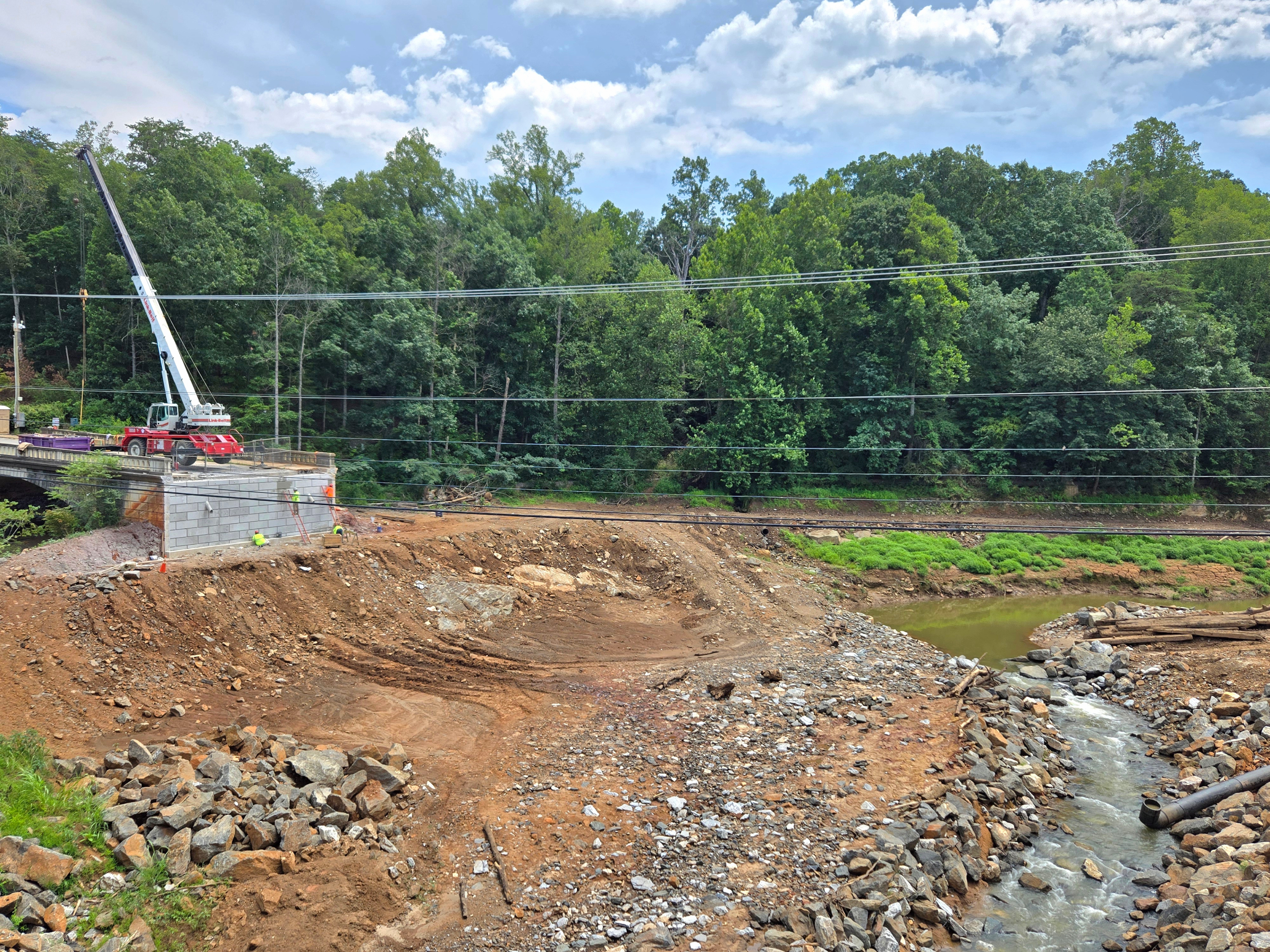 A portion of an old bridge sticks out over a hillside, overlooking a construction site.
