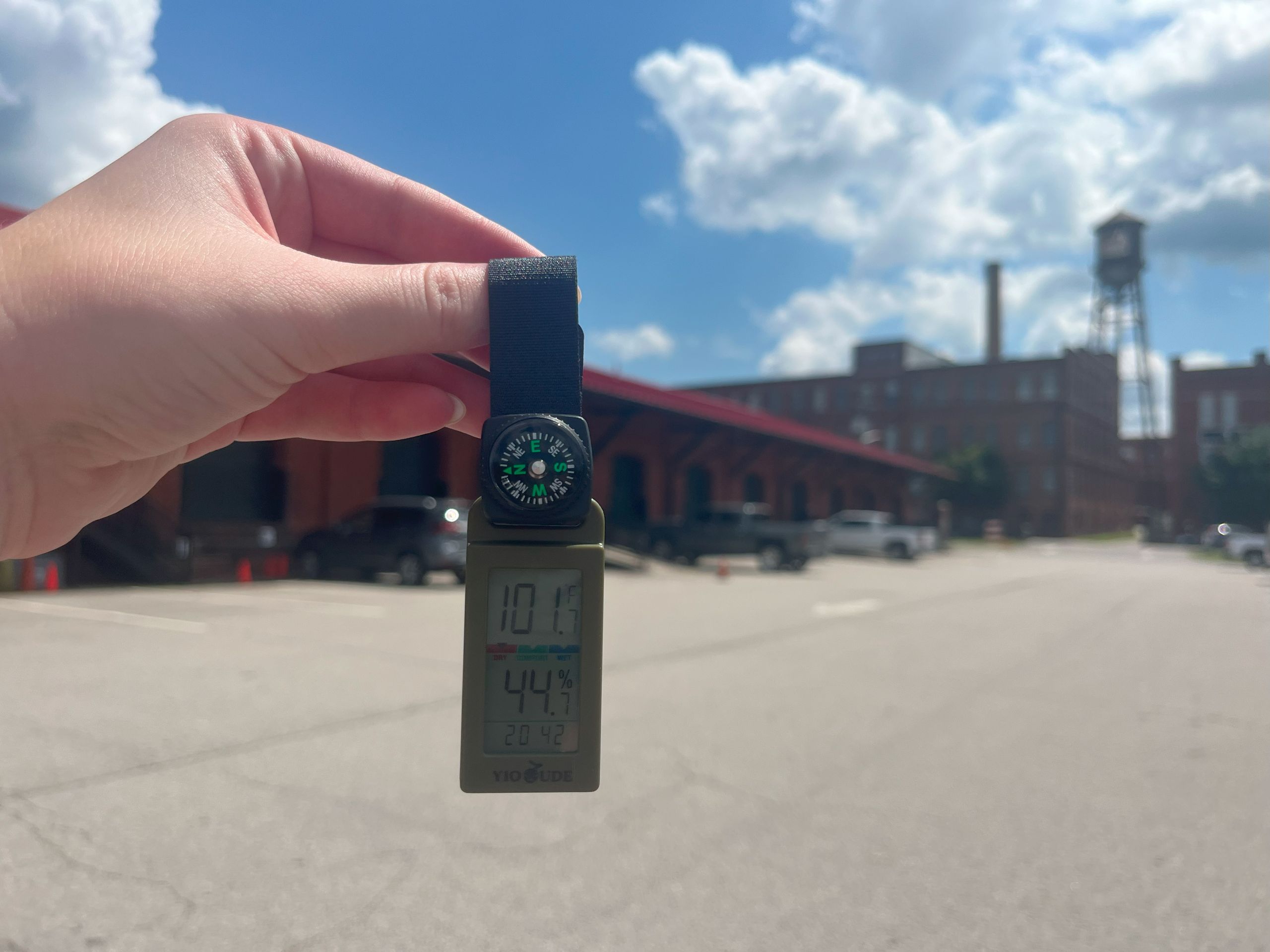 A hand holding up a temperature gauge in front of a parking lot and brick warehouse buildings in Danville.