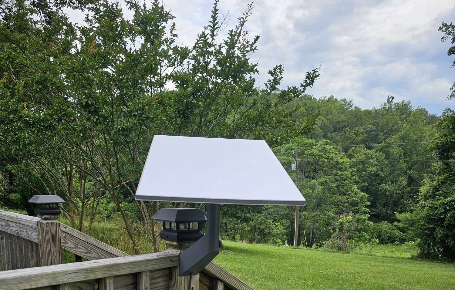 A Starlink satellite dish is shown, attached to a wooden deck facing a verdant back yard.