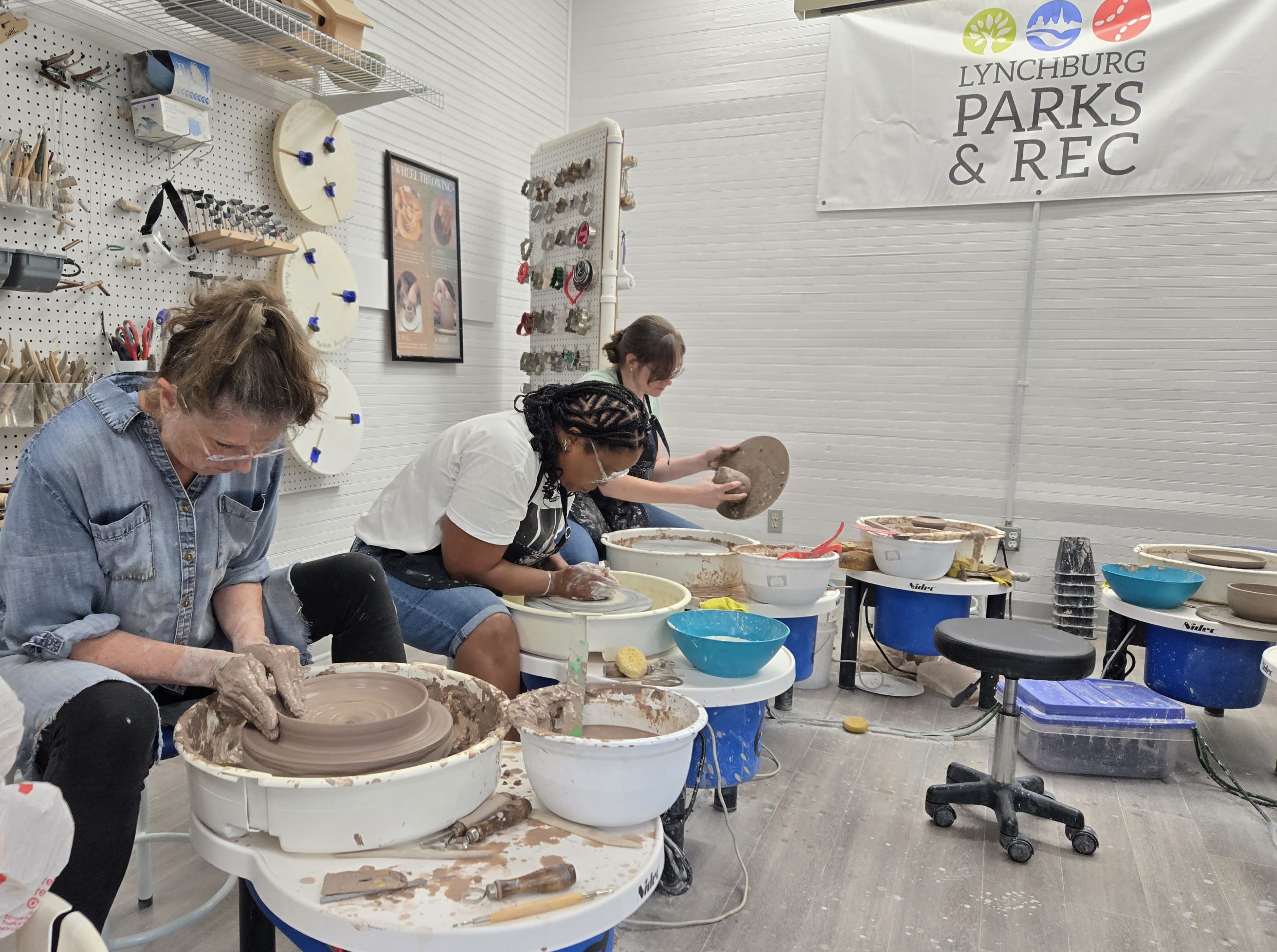 Three women shape bowls out of clay on pottery wheels.