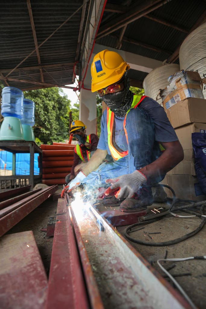 Man in Blue Shirt and Yellow Hard Hat Welding a Metal