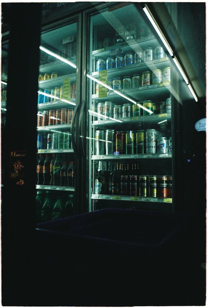 A selection of cans displayed in a brightly lit fridge at night.