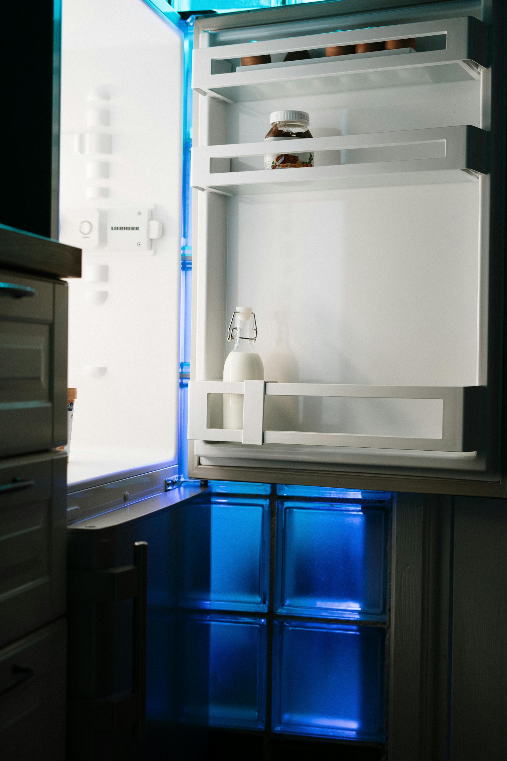An open refrigerator with minimal contents illuminated by neon light in a home kitchen.