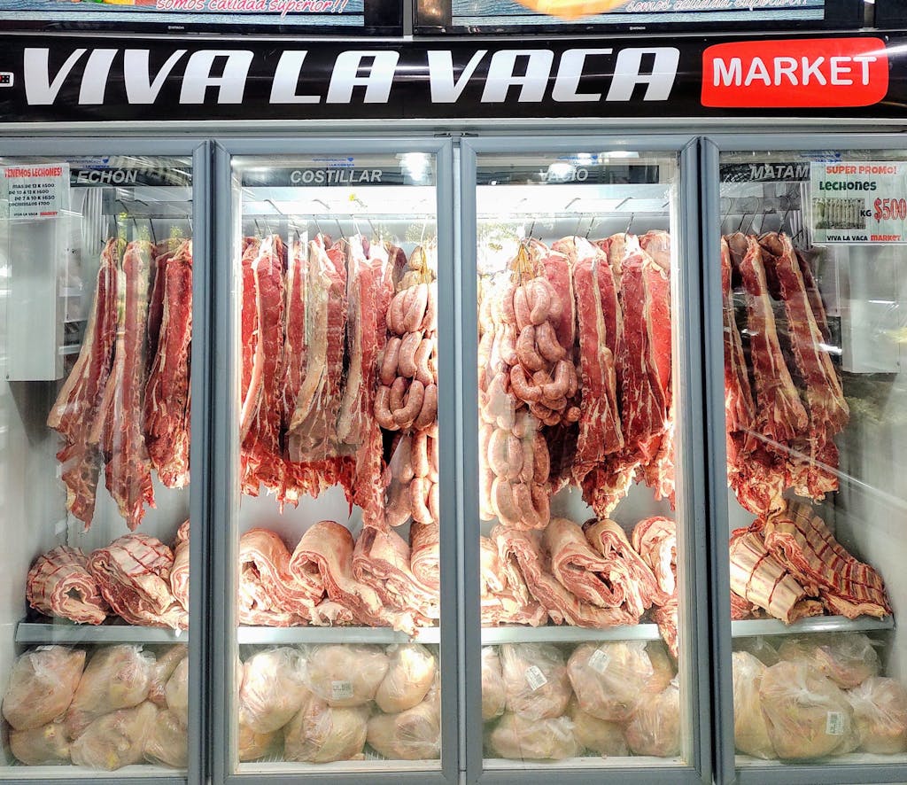 Fresh cuts of meat and sausages in a well-lit market refrigerator display.