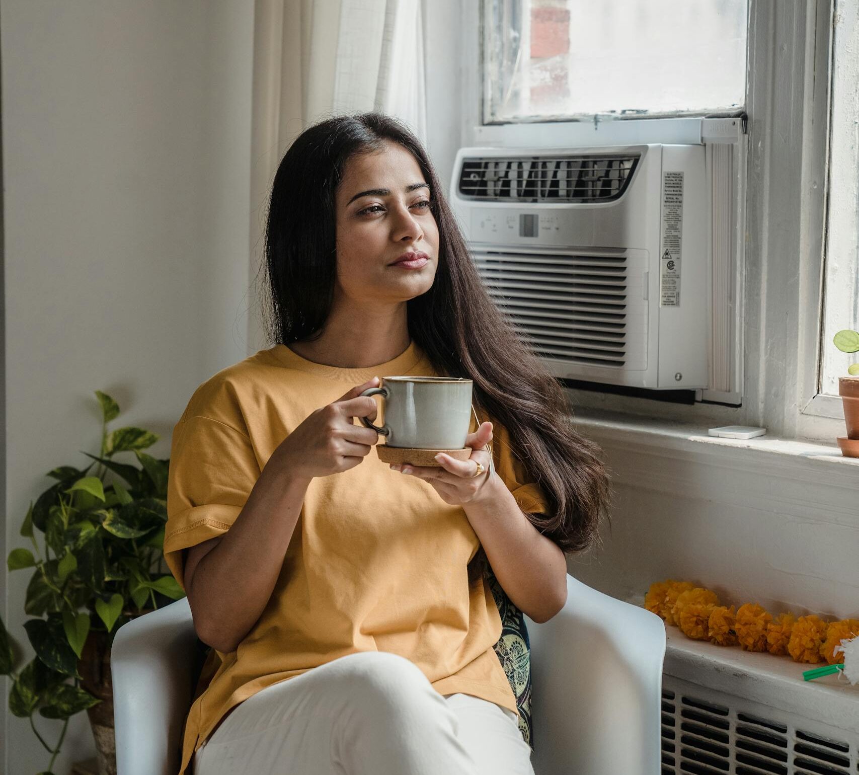South Asian woman sitting indoors, sipping tea and relaxing by the window.