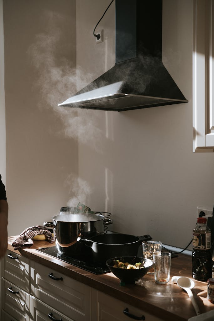 Sunlight illuminates a modern kitchen with steam rising from pots under a range hood.
