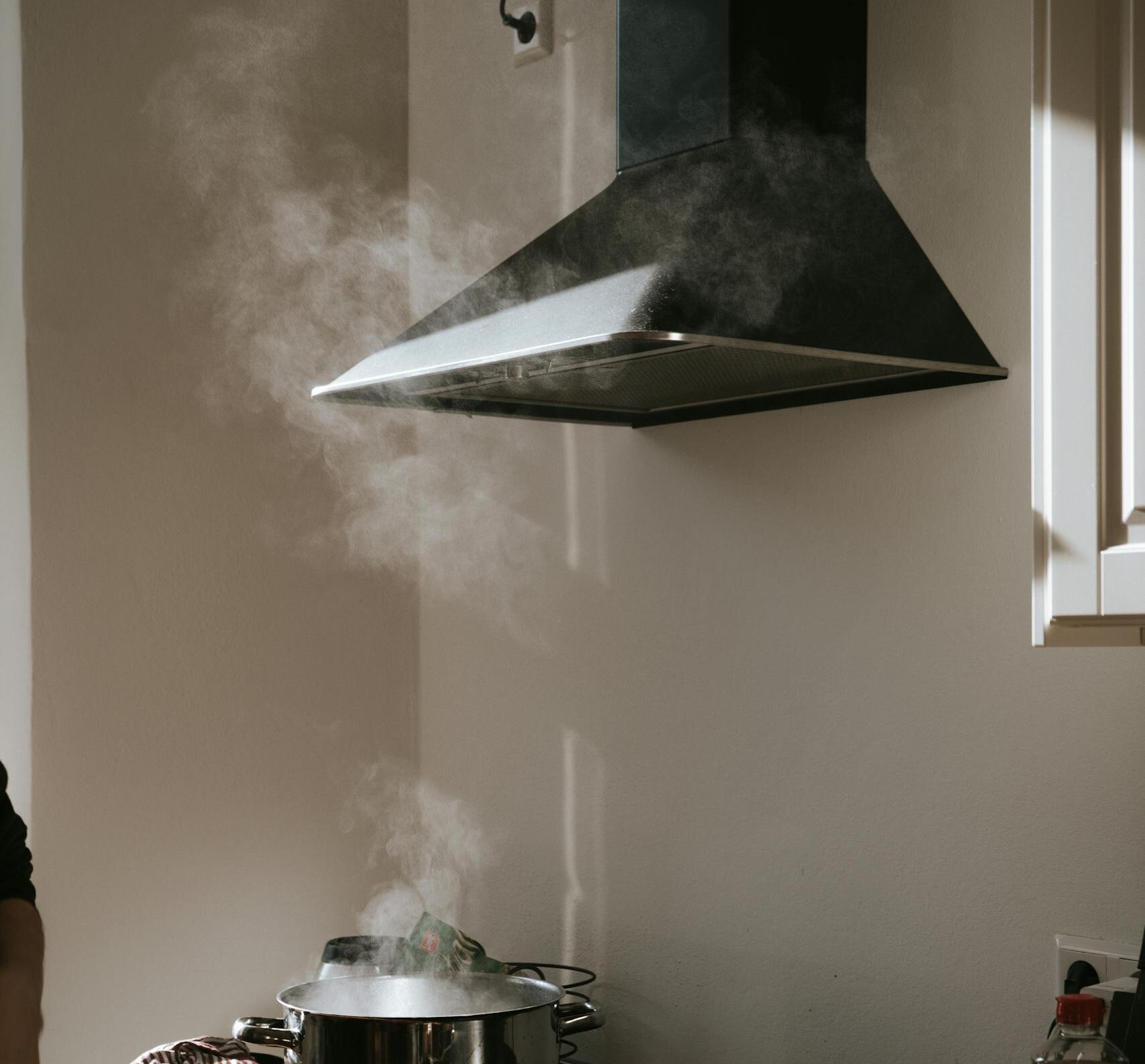 Sunlight illuminates a modern kitchen with steam rising from pots under a range hood.