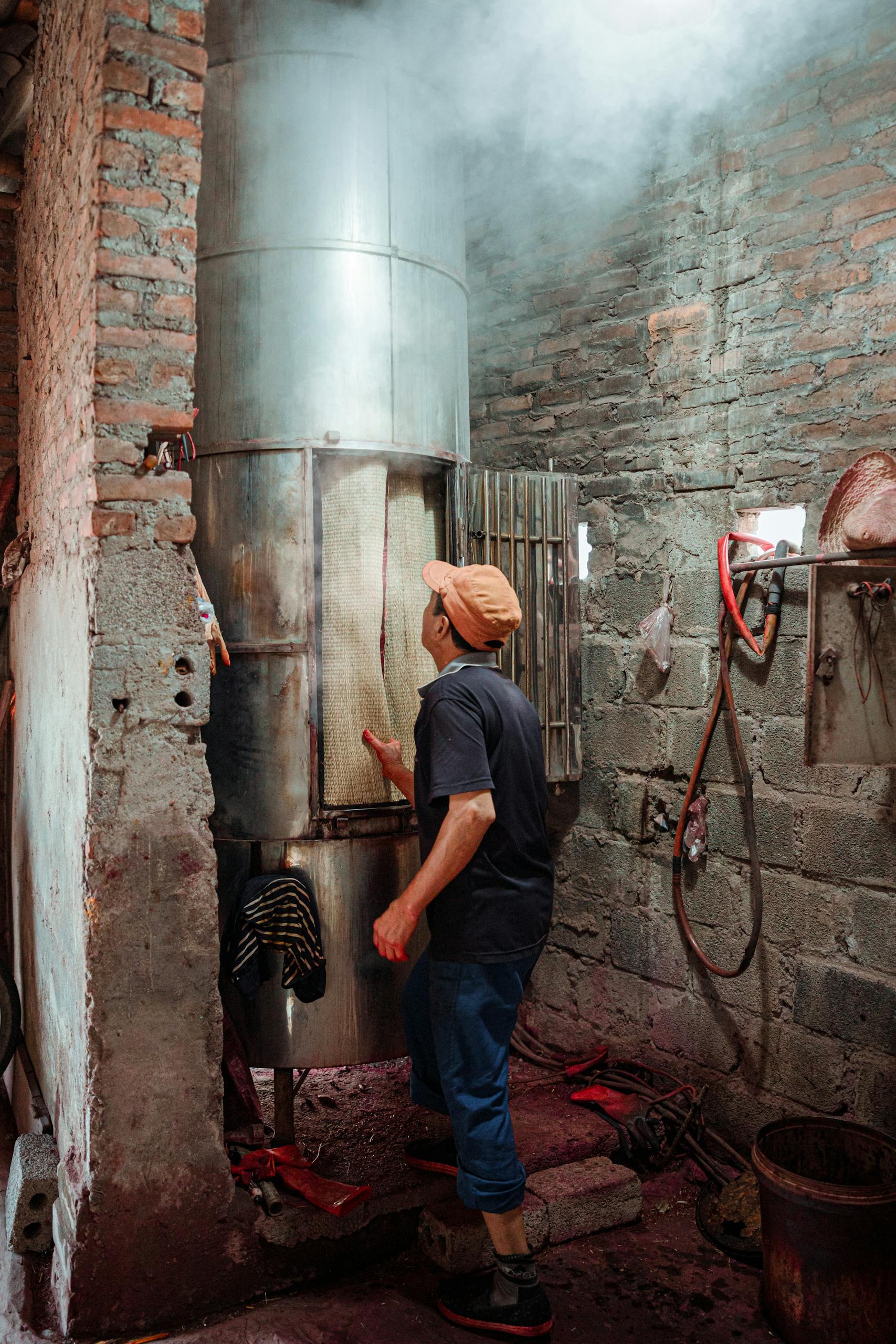 A worker inspects a large industrial metal furnace inside a rustic brick facility.