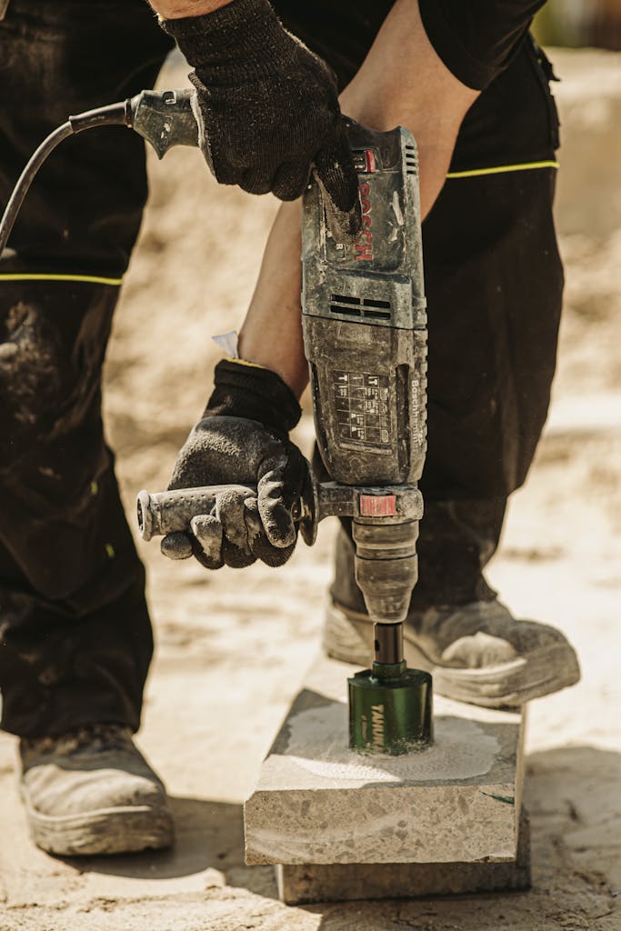 Close-up of a construction worker using a power tool to drill concrete outdoors on a sunny day.